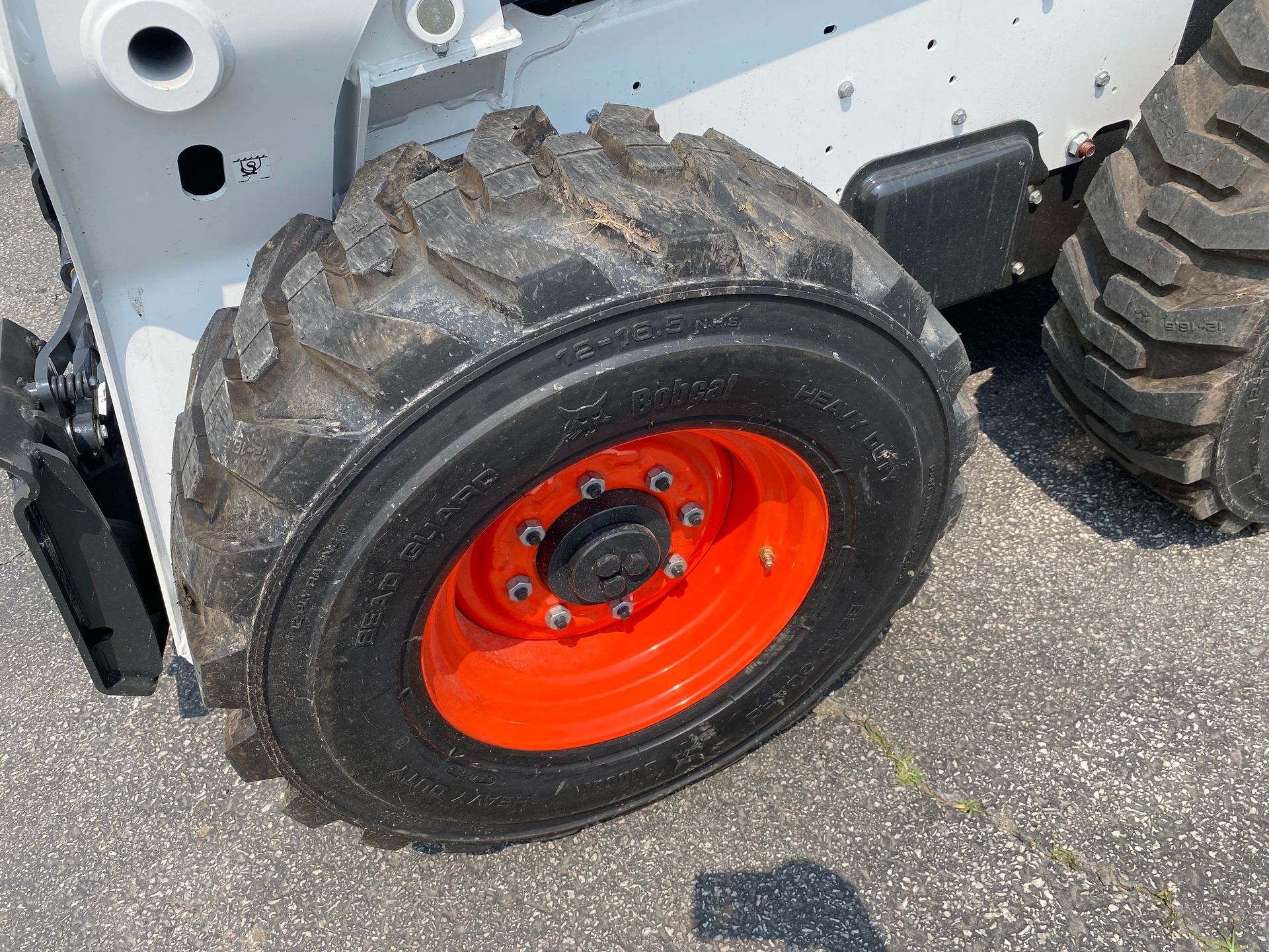 Close-up of a Bobcat skid-steer wheel, black tire on an orange rim, bolts visible.