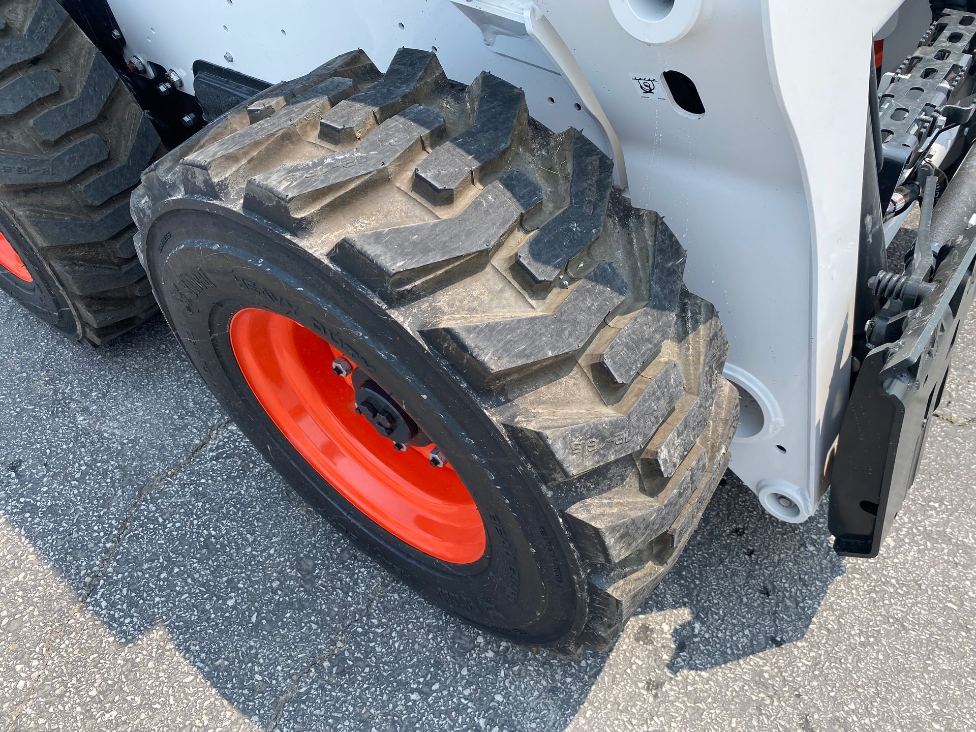 Bobcat skid-steer loader wheel with orange rim and black, treaded tire on gray pavement.