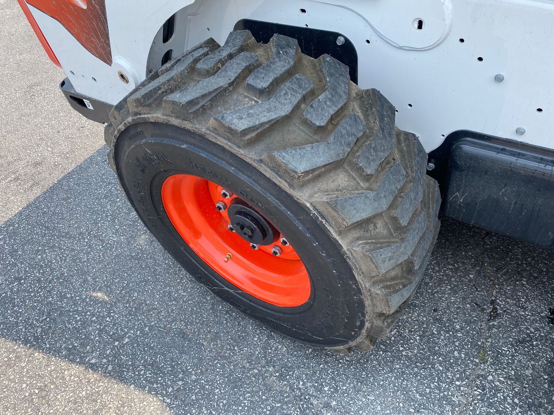 Close-up of a Bobcat skid-steer loader wheel with an orange rim and black, heavily treaded tire on asphalt.