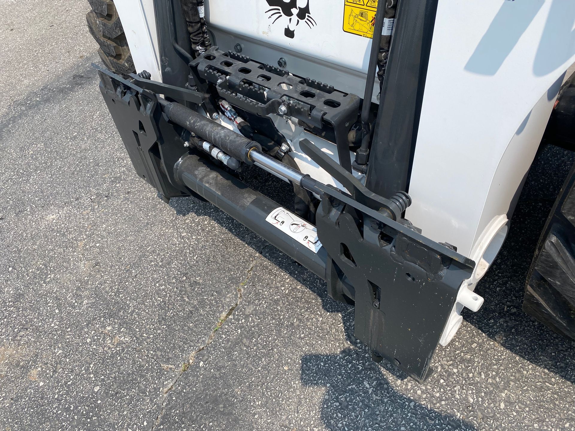 Close-up of Bobcat skid steer attachment. Black metal frame, hydraulic cylinder, and white machine.