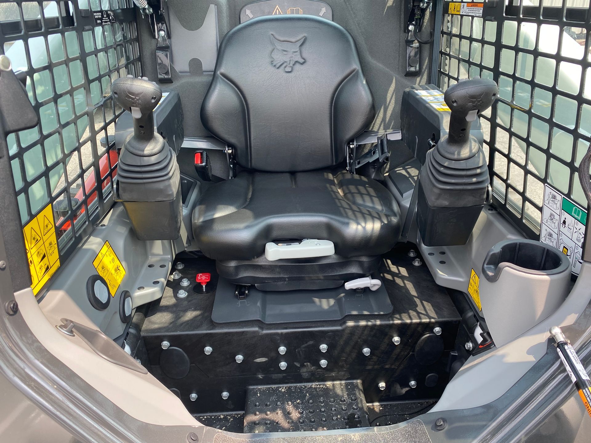 Interior of a Bobcat skid steer. Black seat with joysticks, safety cage, and cup holder.