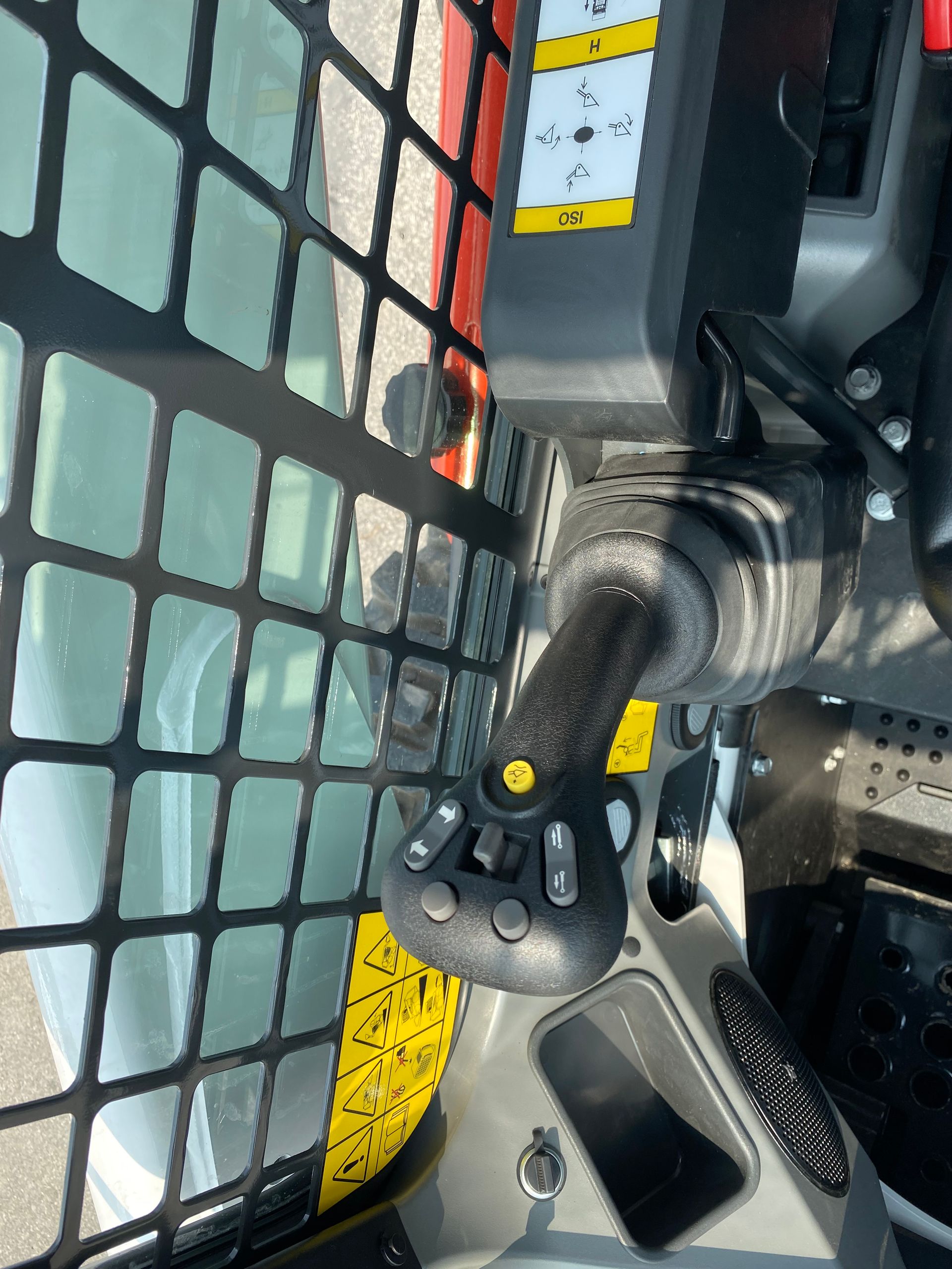 Close-up of a skid steer joystick. Black joystick with buttons, in a cab next to a safety screen.