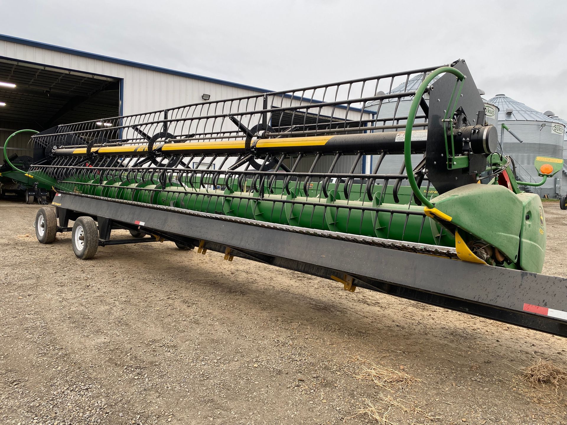 John Deere combine header on a trailer, green and black, outdoors.