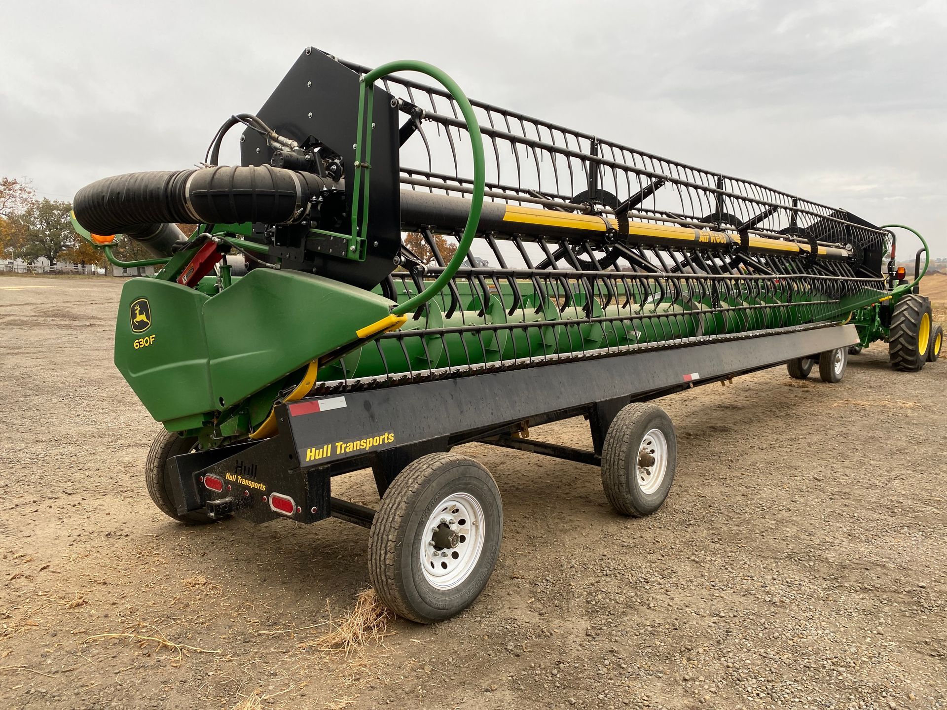 John Deere combine header on a trailer, in a field, with a green and black color scheme.