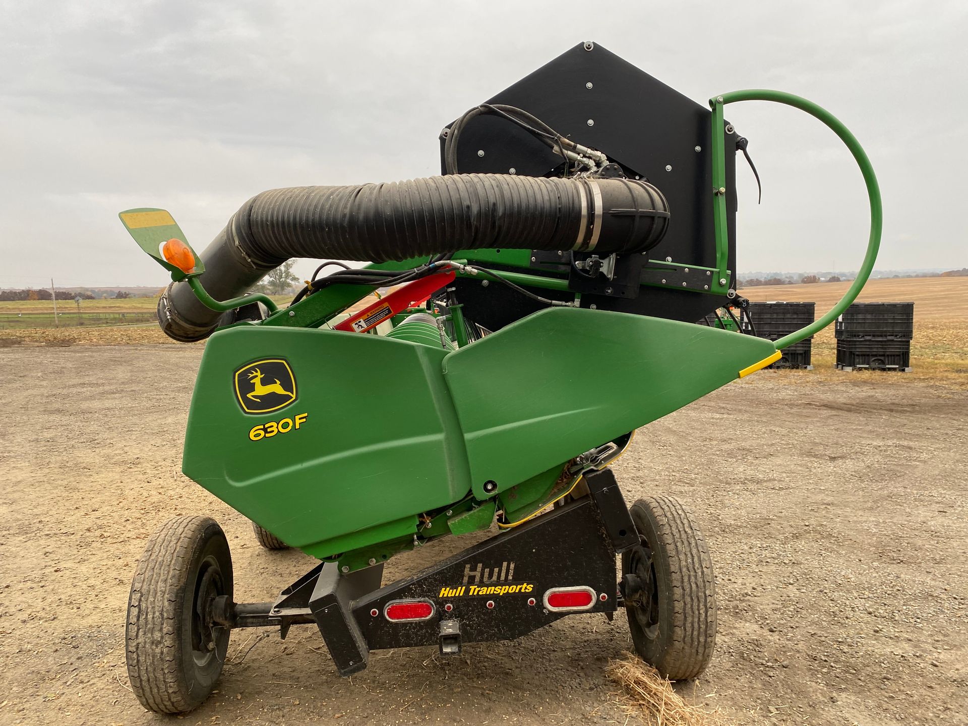 John Deere K925L harvest machine, green, black, and orange, in a field, under a cloudy sky.