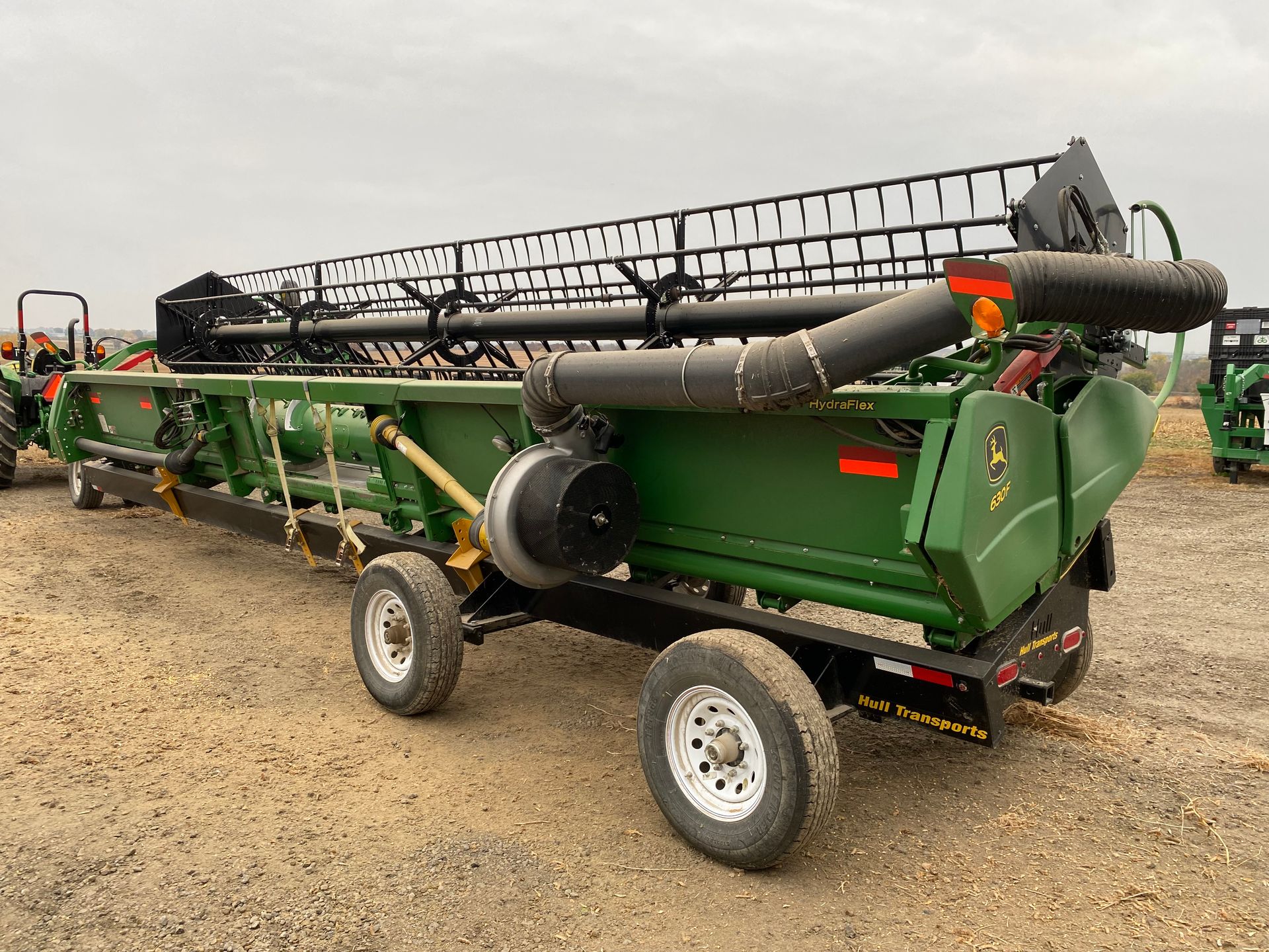 Green John Deere combine header on a trailer, outdoors.