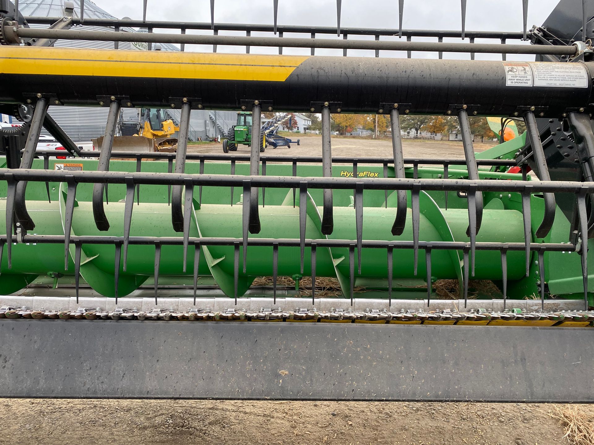 Green and black combine header, with a large auger, outside.