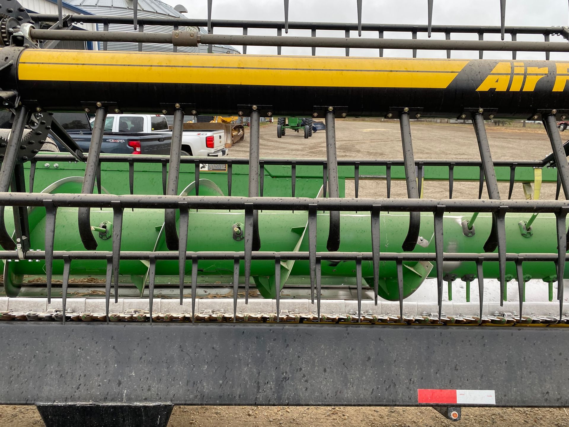 Close-up of a green and yellow combine header with tines, used for harvesting crops.