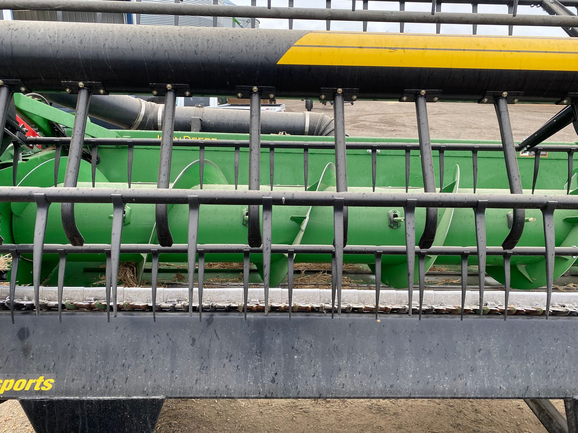 Green and black combine header with augers and tines, likely for harvesting crops.