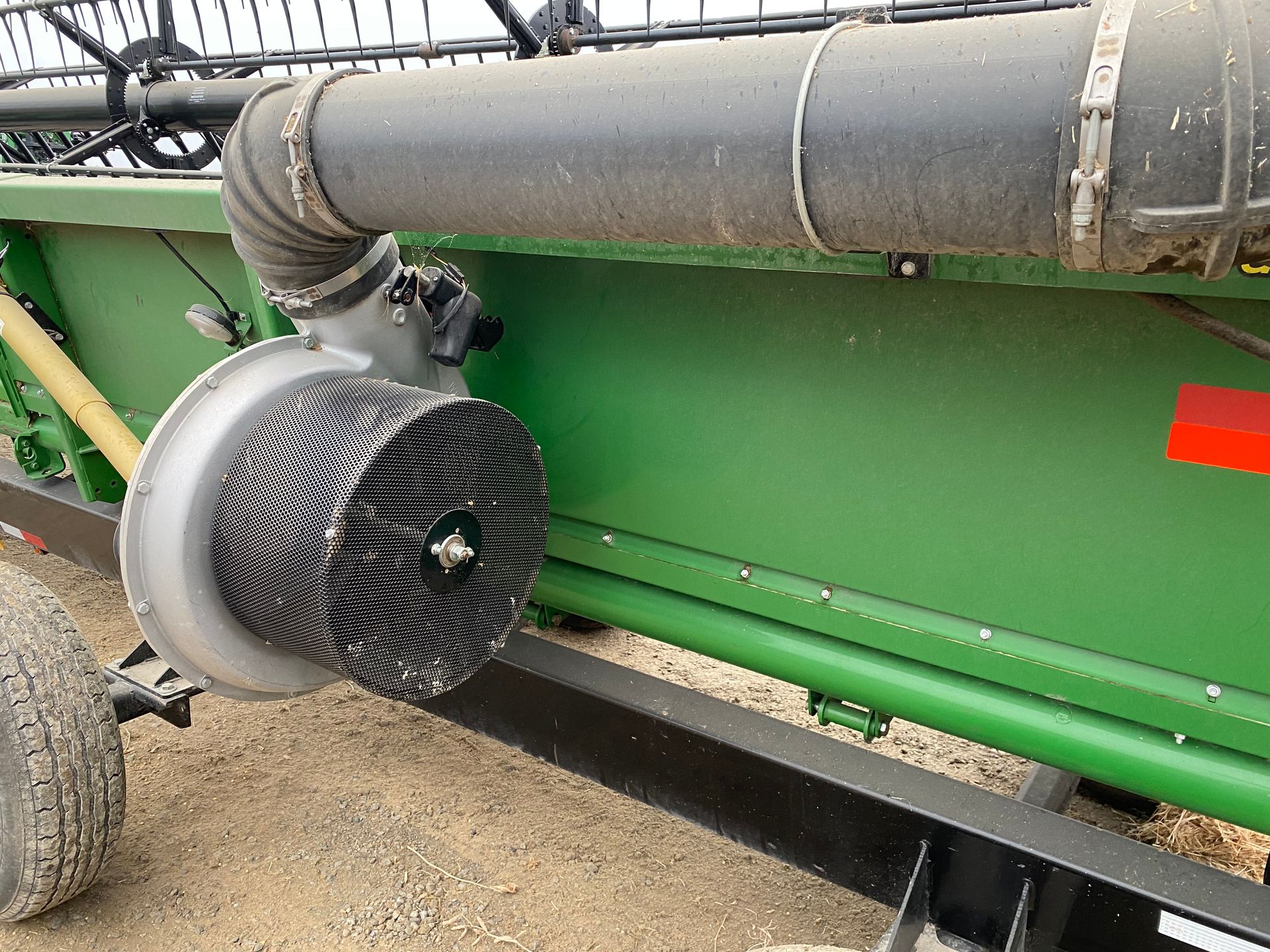 Combine fan with rotating brushes, connected to a black hose, mounted on a green grain cart.