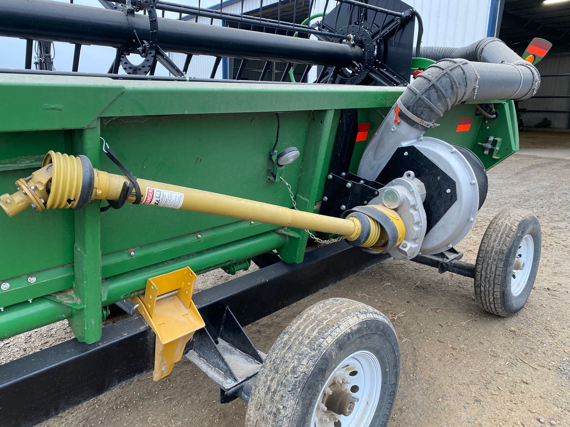 Green and black farm implement with a yellow driveshaft and white wheels.