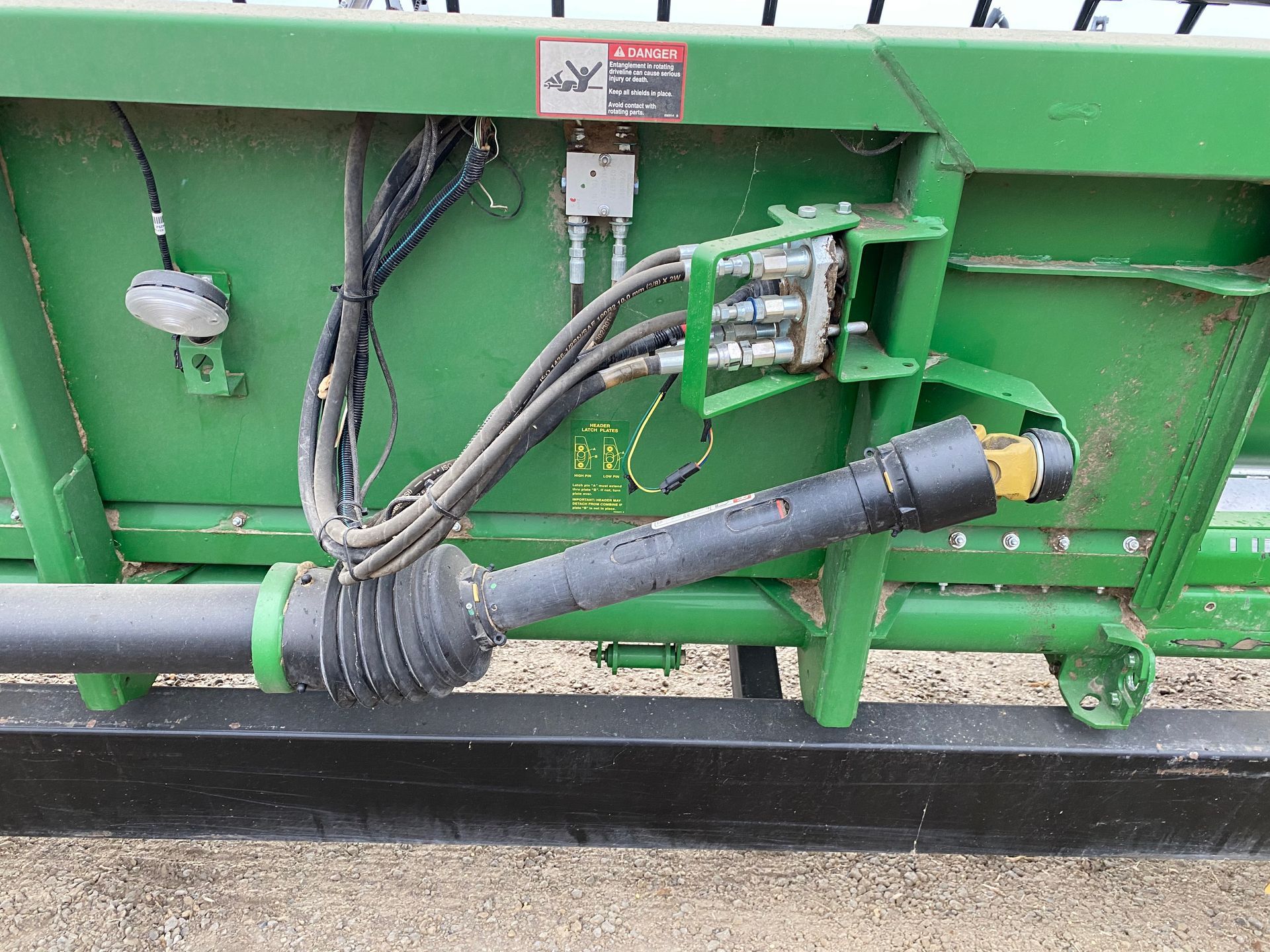 Green farm implement with a black drive shaft, hoses, and hydraulic components.