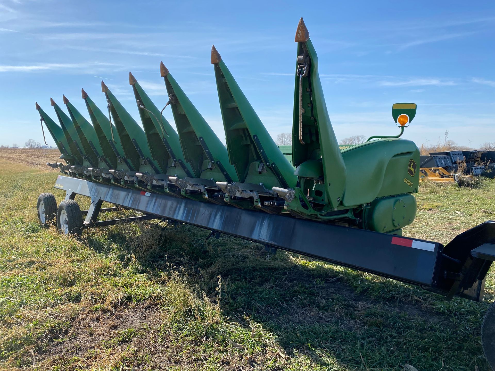 Green John Deere corn header on a trailer, in a field.