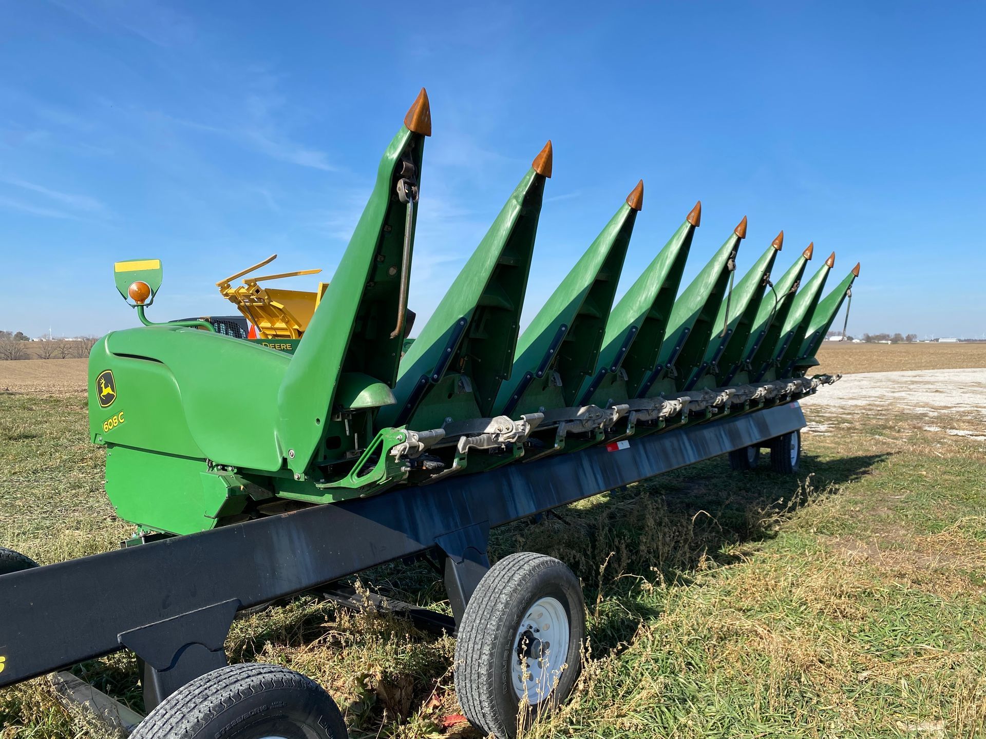 Green corn header, attached to a cart, in a field, under a blue sky.