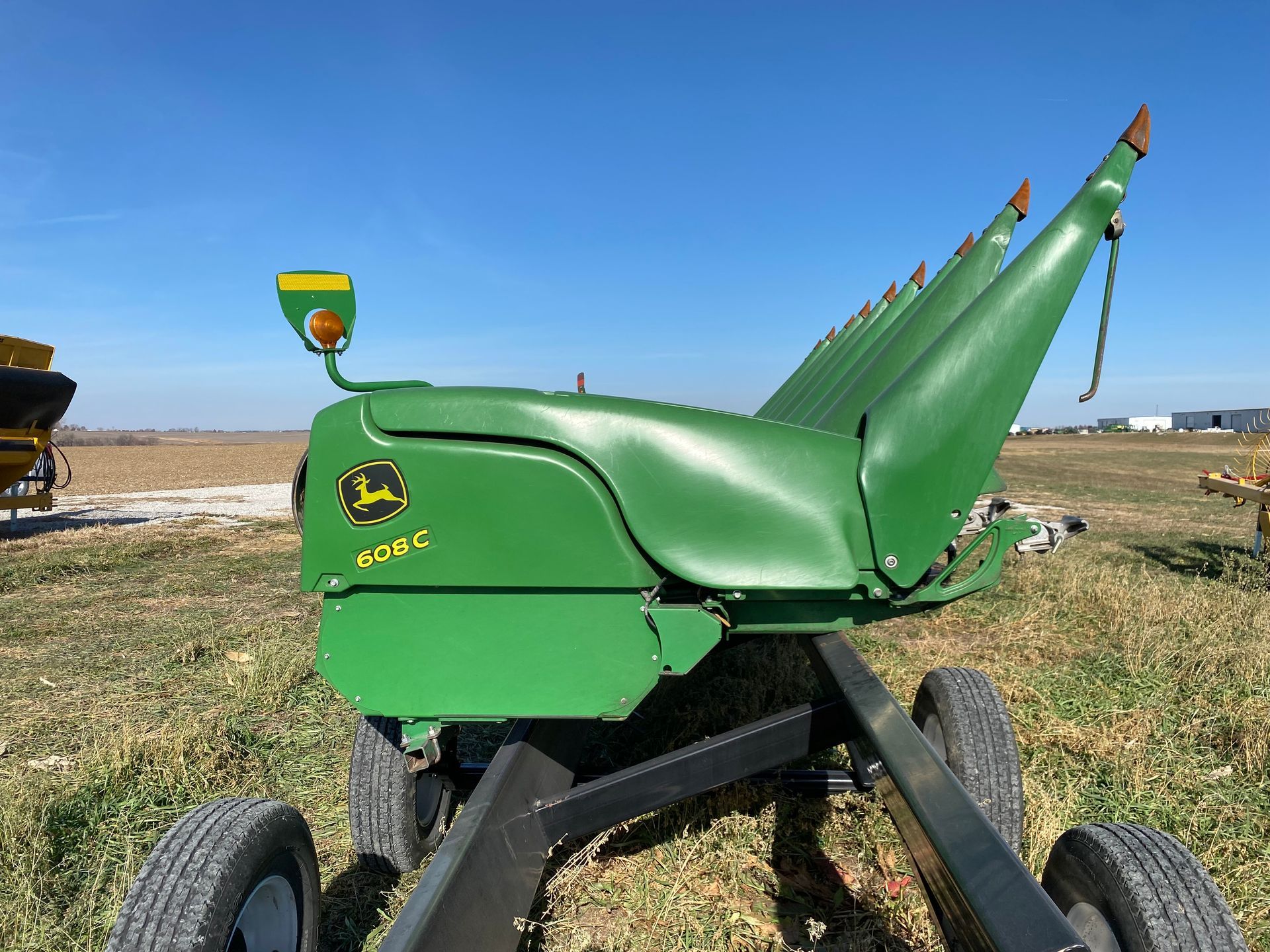 Green John Deere corn head in a field on a sunny day.