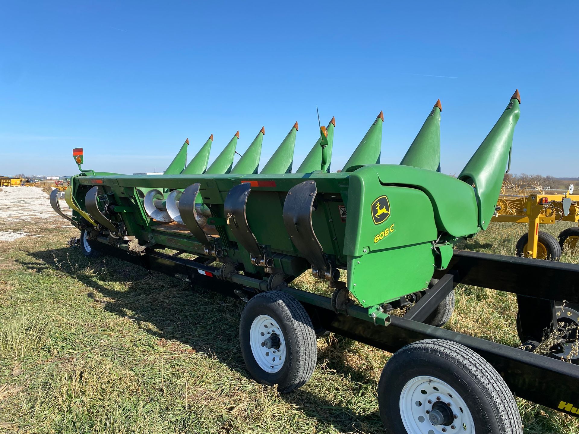 Green John Deere corn head on a black trailer in a field on a sunny day.