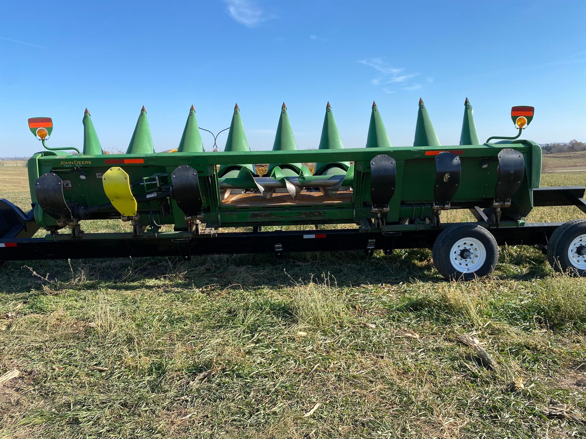 Green corn header on a trailer, in a field under a blue sky.