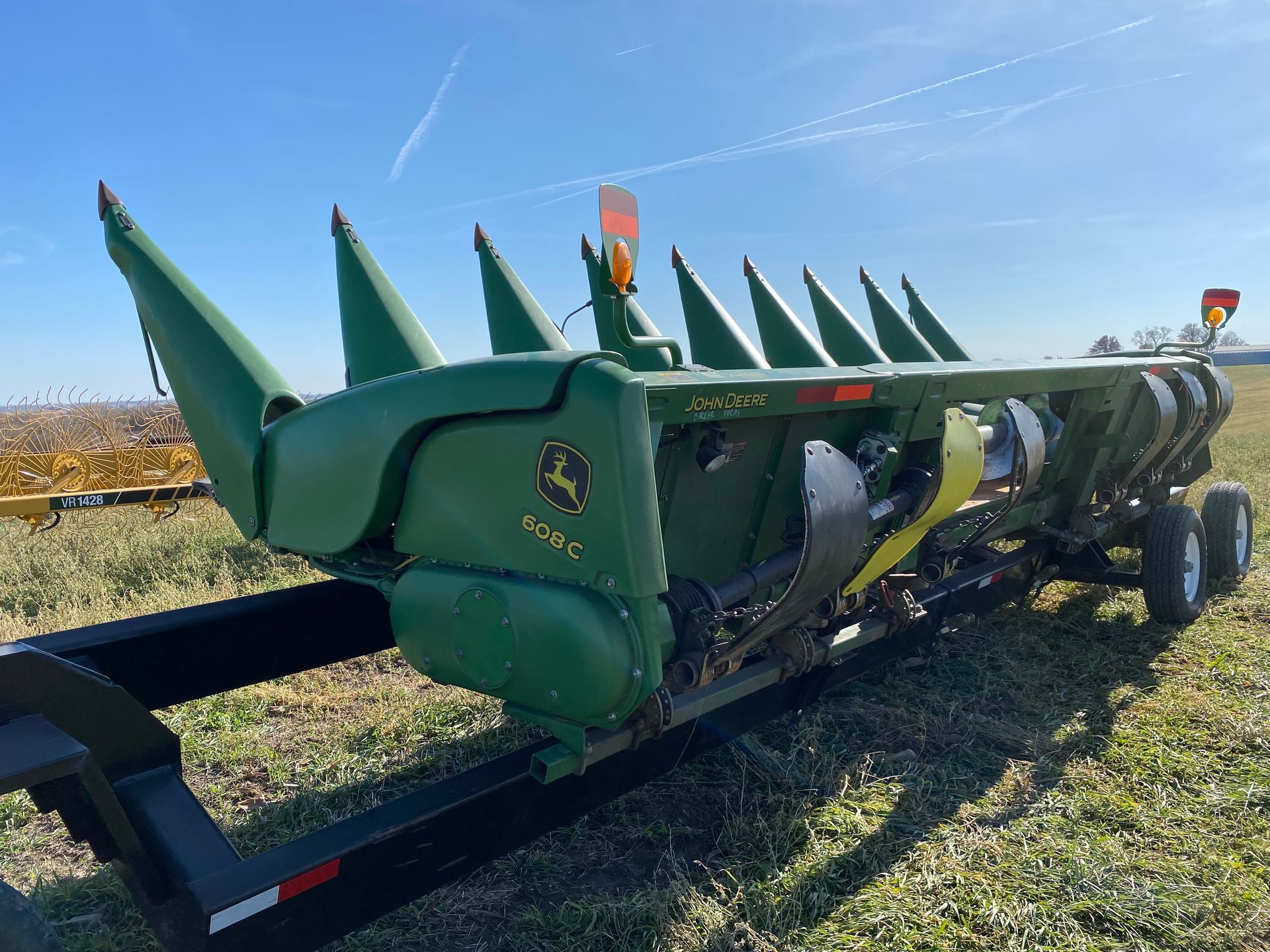 Green John Deere corn head on a trailer in a field, under a blue sky.