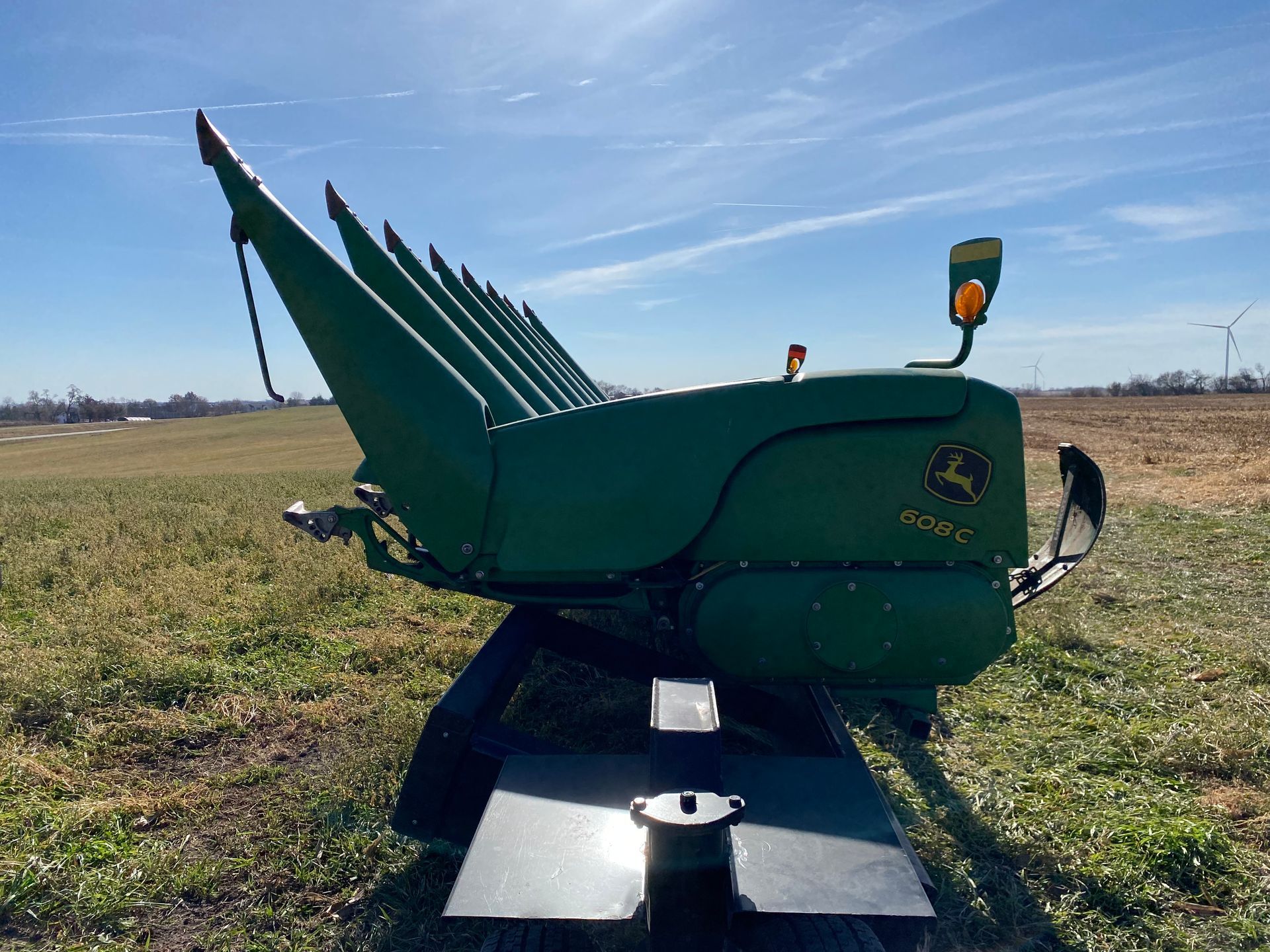 Green John Deere corn head in a field under a blue sky.