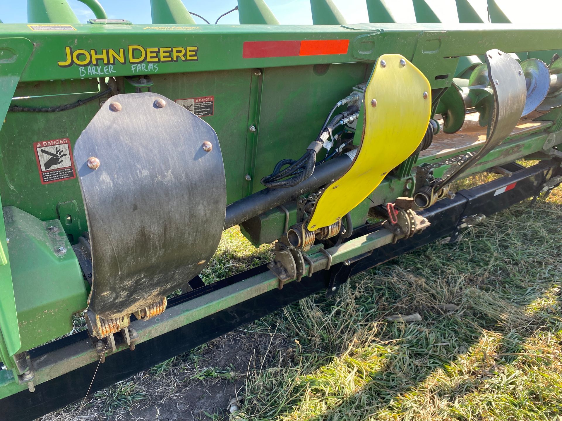 A John Deere corn head attachment. Green and yellow metal with silver guards, outdoors.