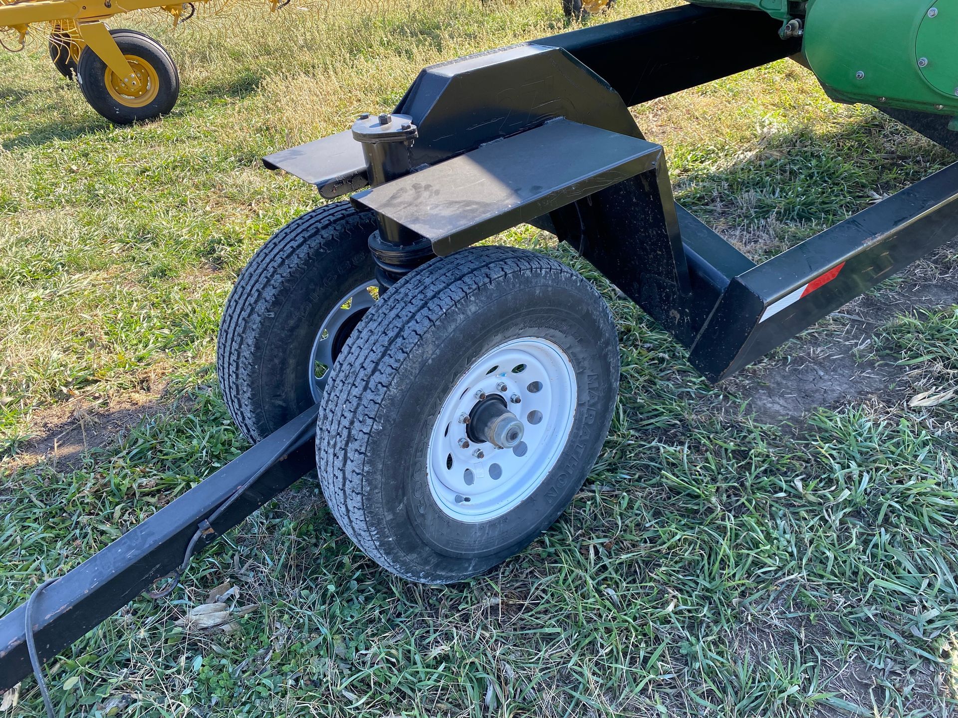 Black farm equipment trailer with two tires on grass.