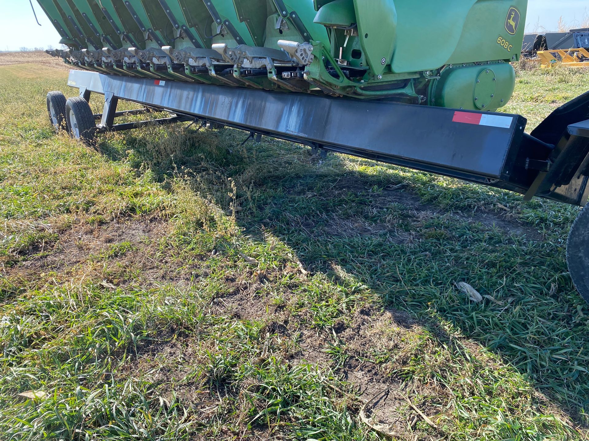 A large green agricultural header trailer parked in a grassy field.