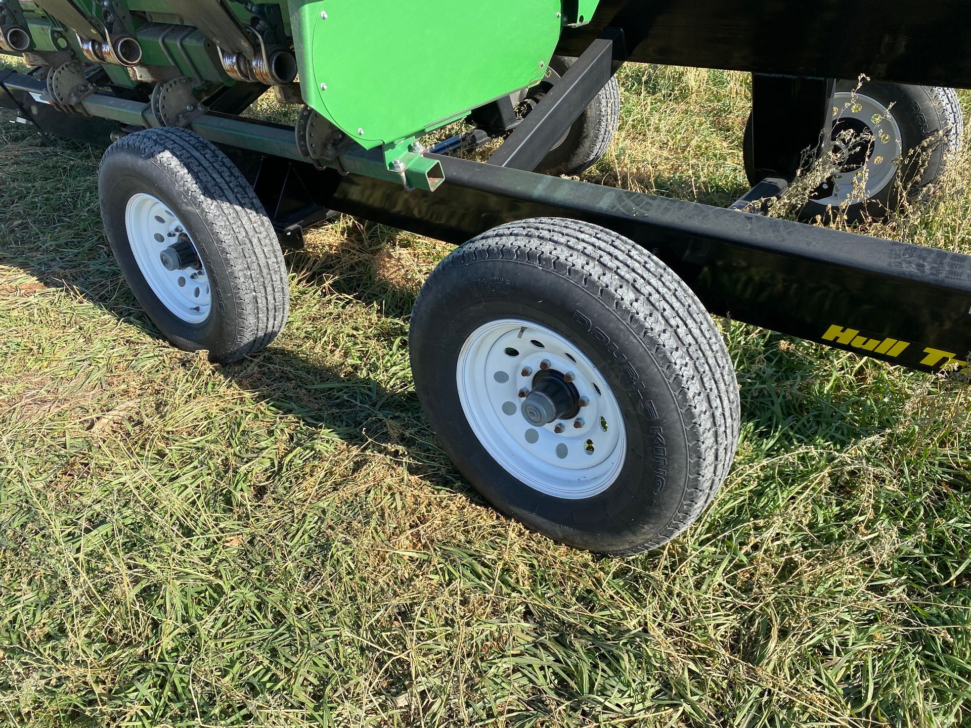 A green corn head on a grassy field with two white-rimmed tires.