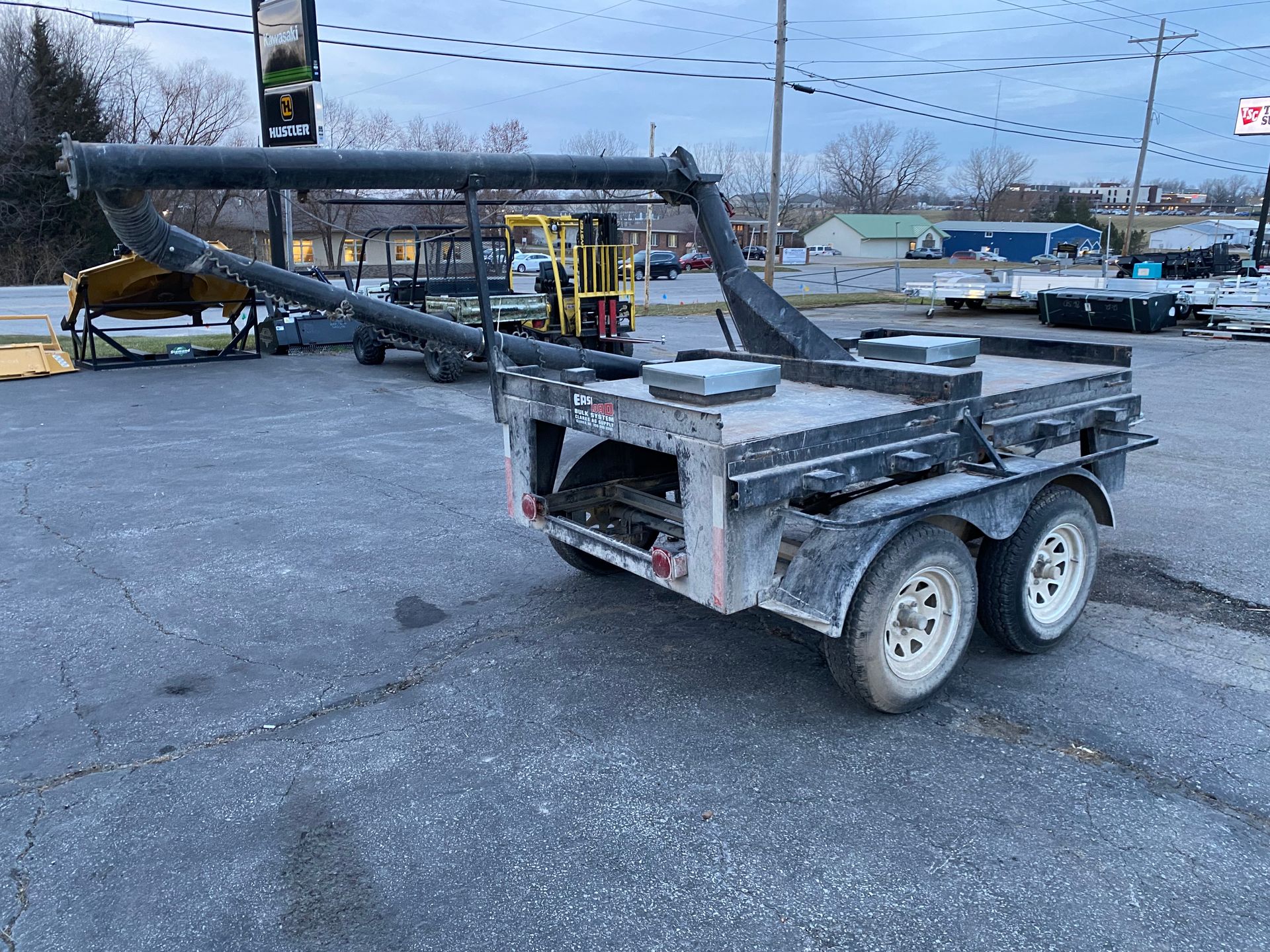Black utility trailer with dual wheels parked on pavement; cloudy day.