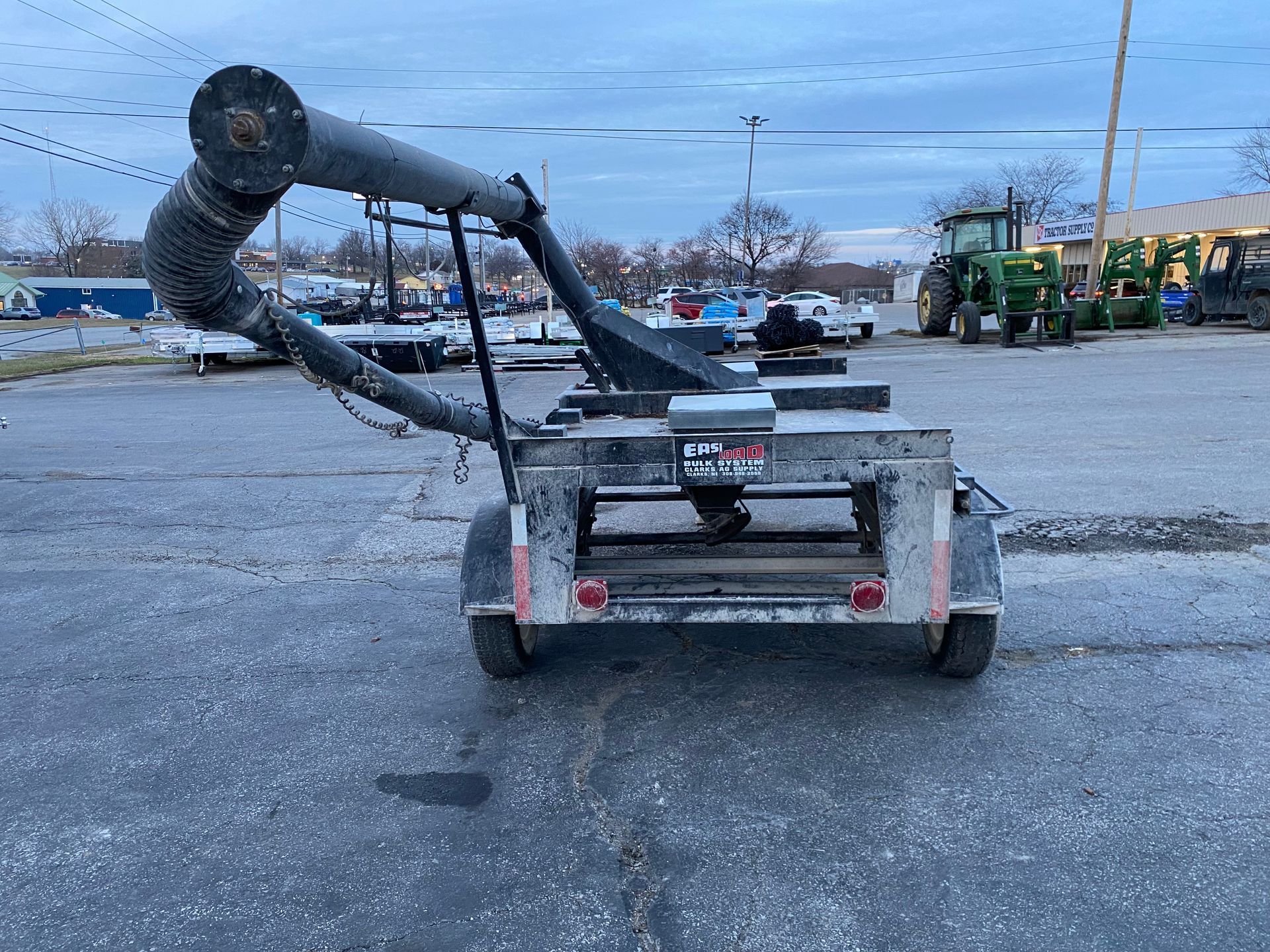 Grain auger on trailer, parked outside on asphalt. Gray cloudy sky in background.