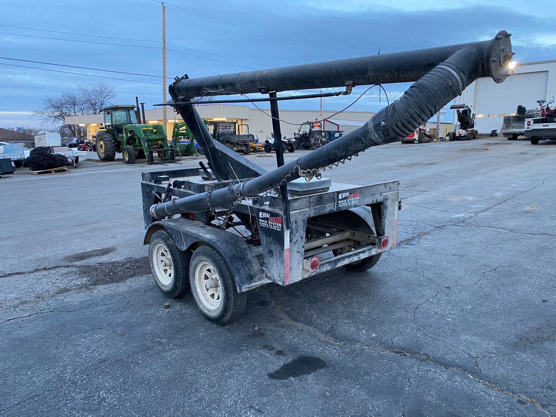 A trailer with a large, black, angled tube attached, possibly for agricultural use, in a lot.