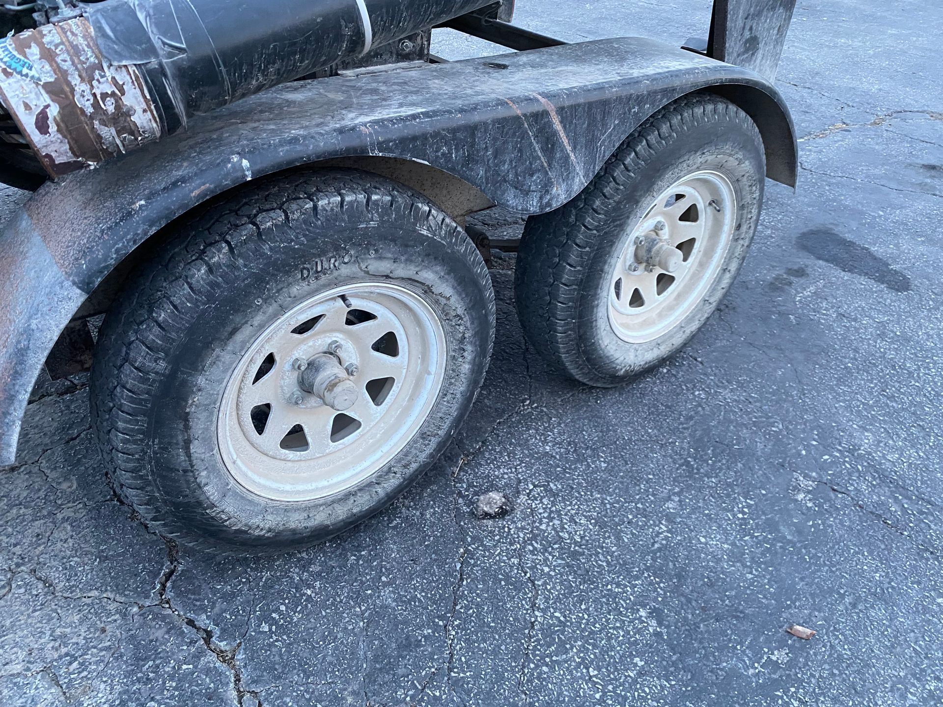 Two dirty trailer tires with white rims and a black fender.