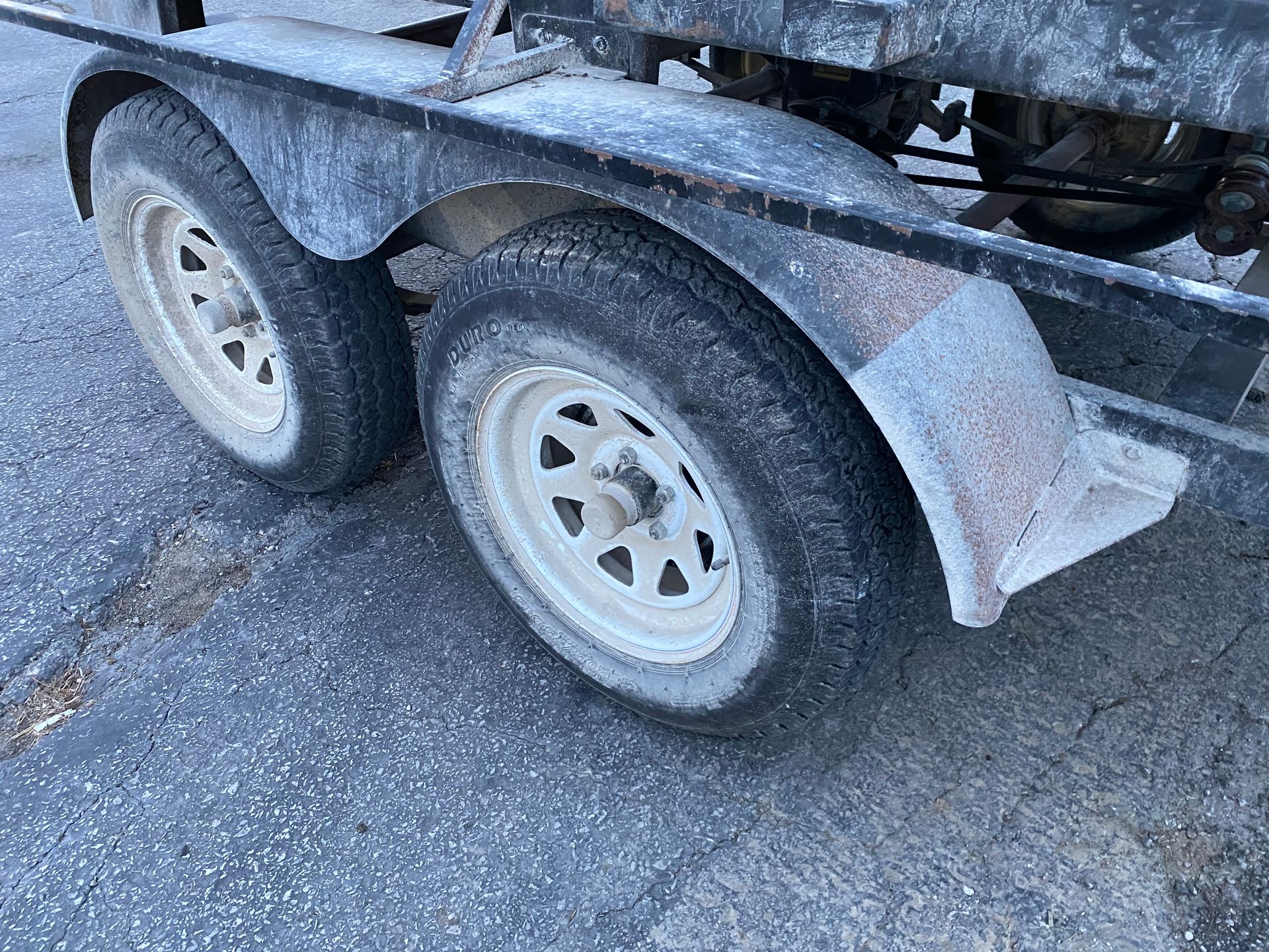 Two trailer tires with white rims and a black fender, covered in a white substance.