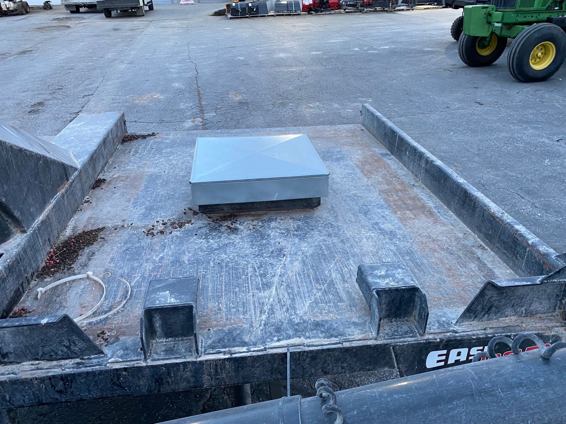 Metal box on a weathered gray flatbed trailer, with a tractor visible in the background.
