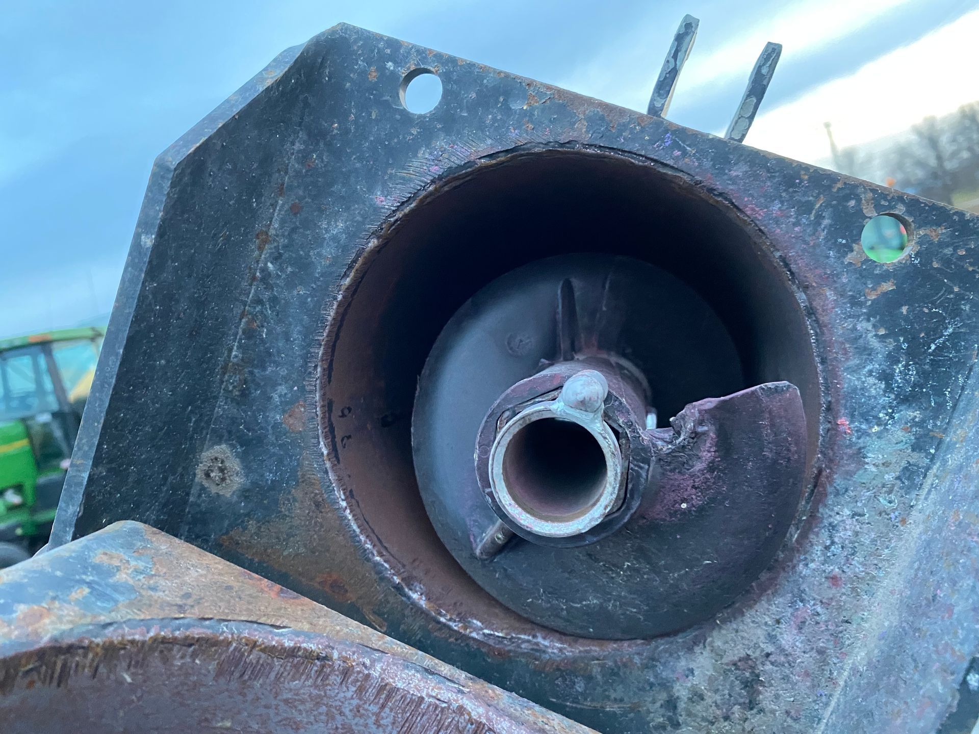 Close-up of a damaged auger inside a black metal housing, likely part of farm equipment.