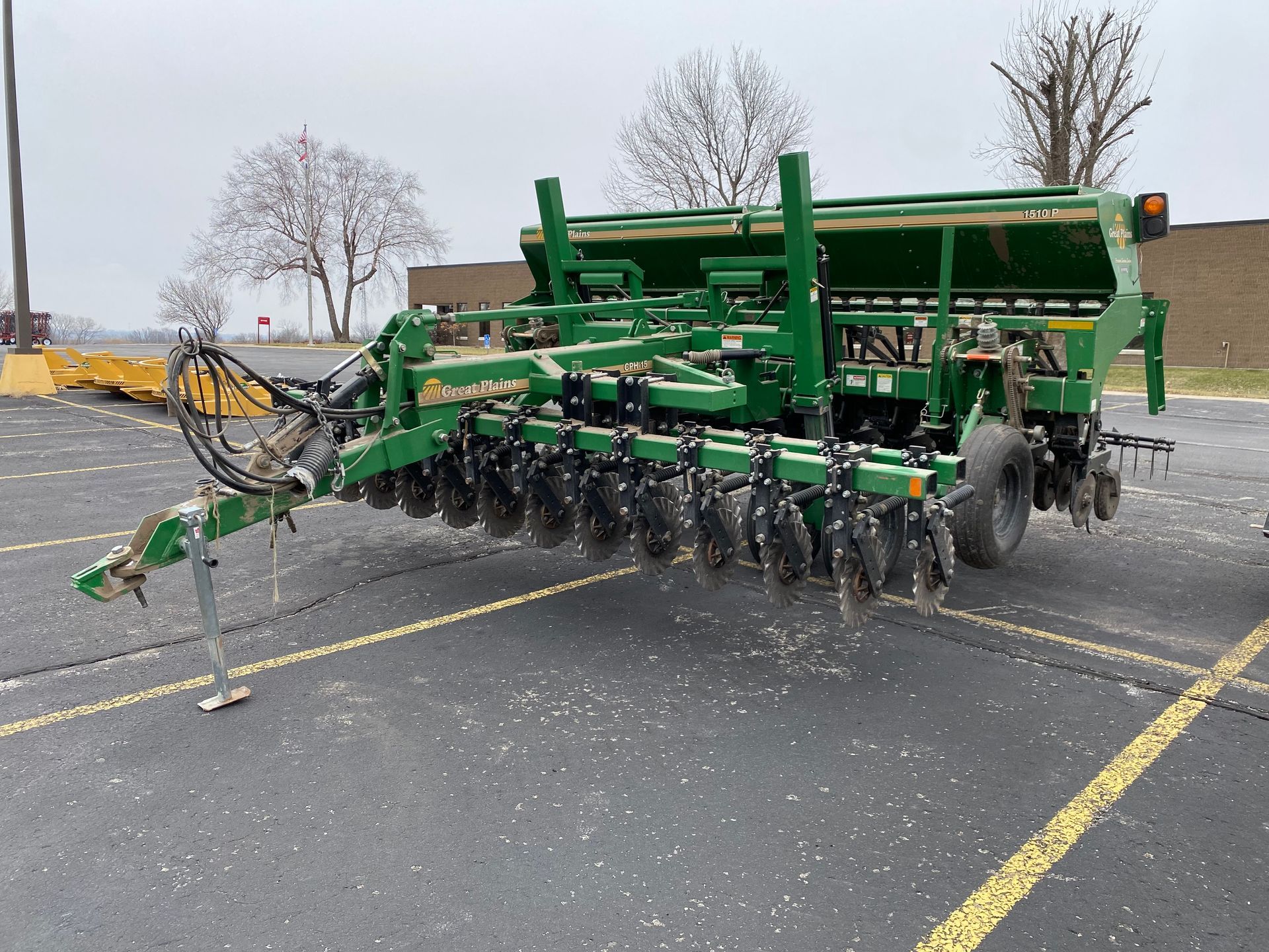 Green and black farm drill on asphalt lot.