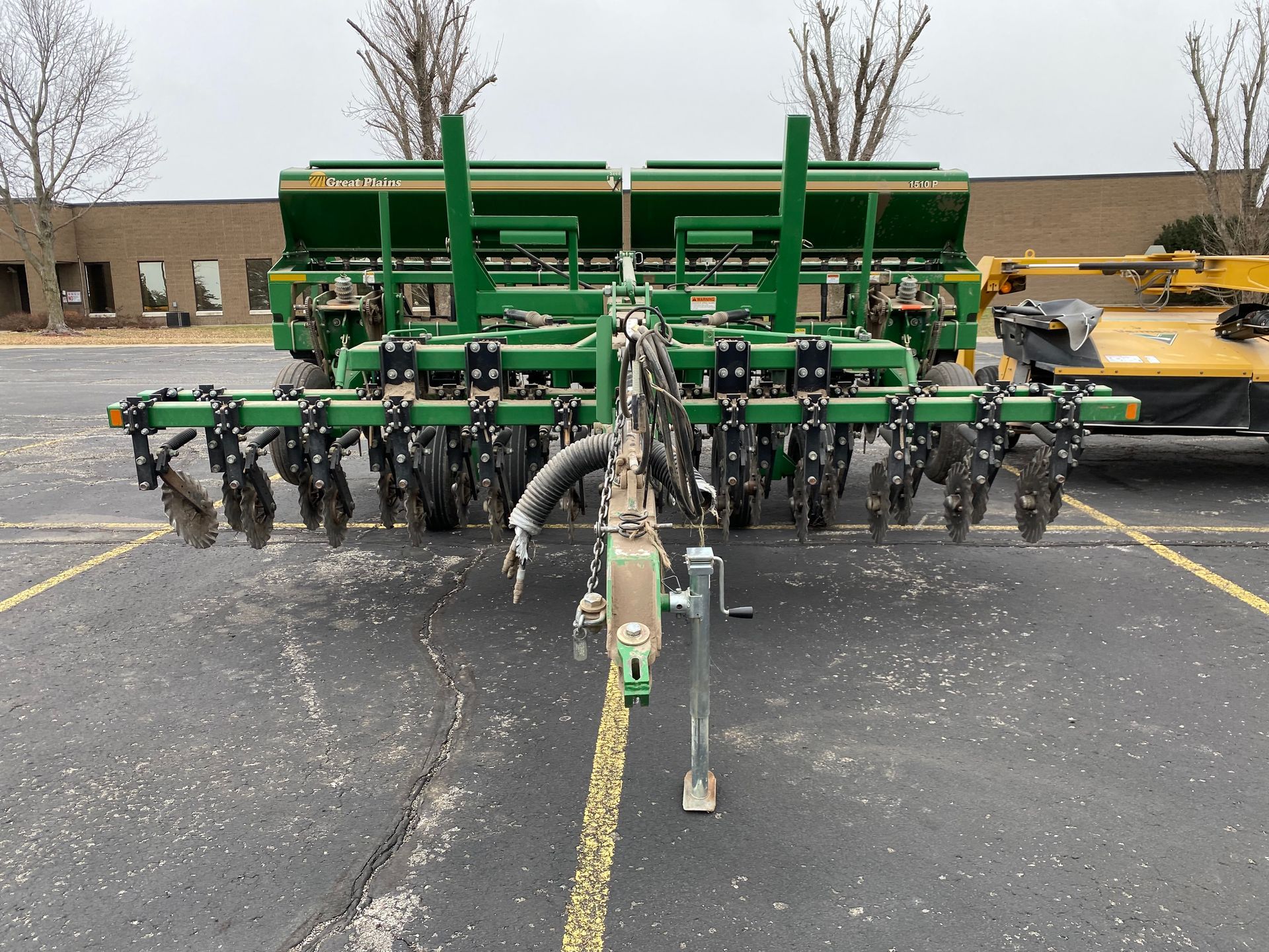 Green agricultural grain drill parked on asphalt, cloudy day, front shot.