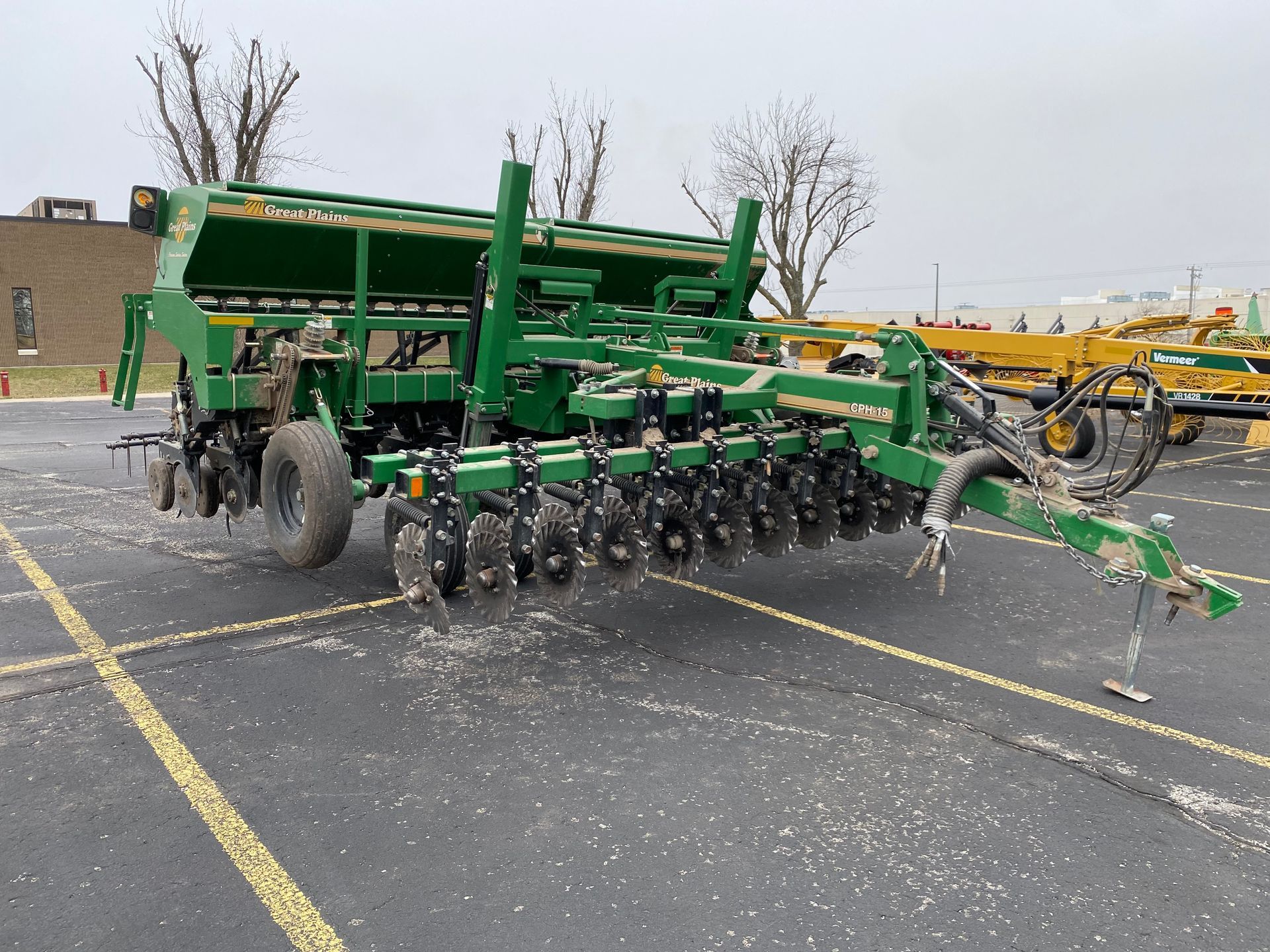 Green agricultural grain drill parked on asphalt, cloudy day, front angled shot.
