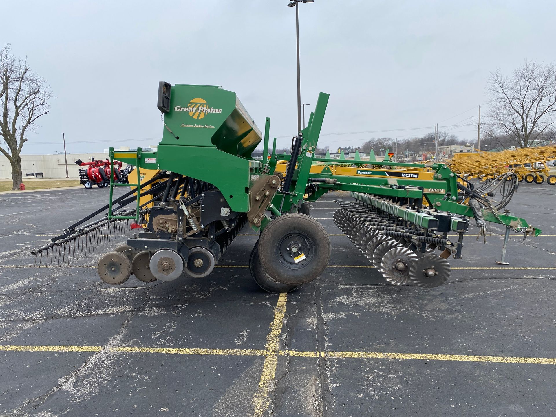 Green agricultural grain drill parked on asphalt, cloudy day, side view shot.