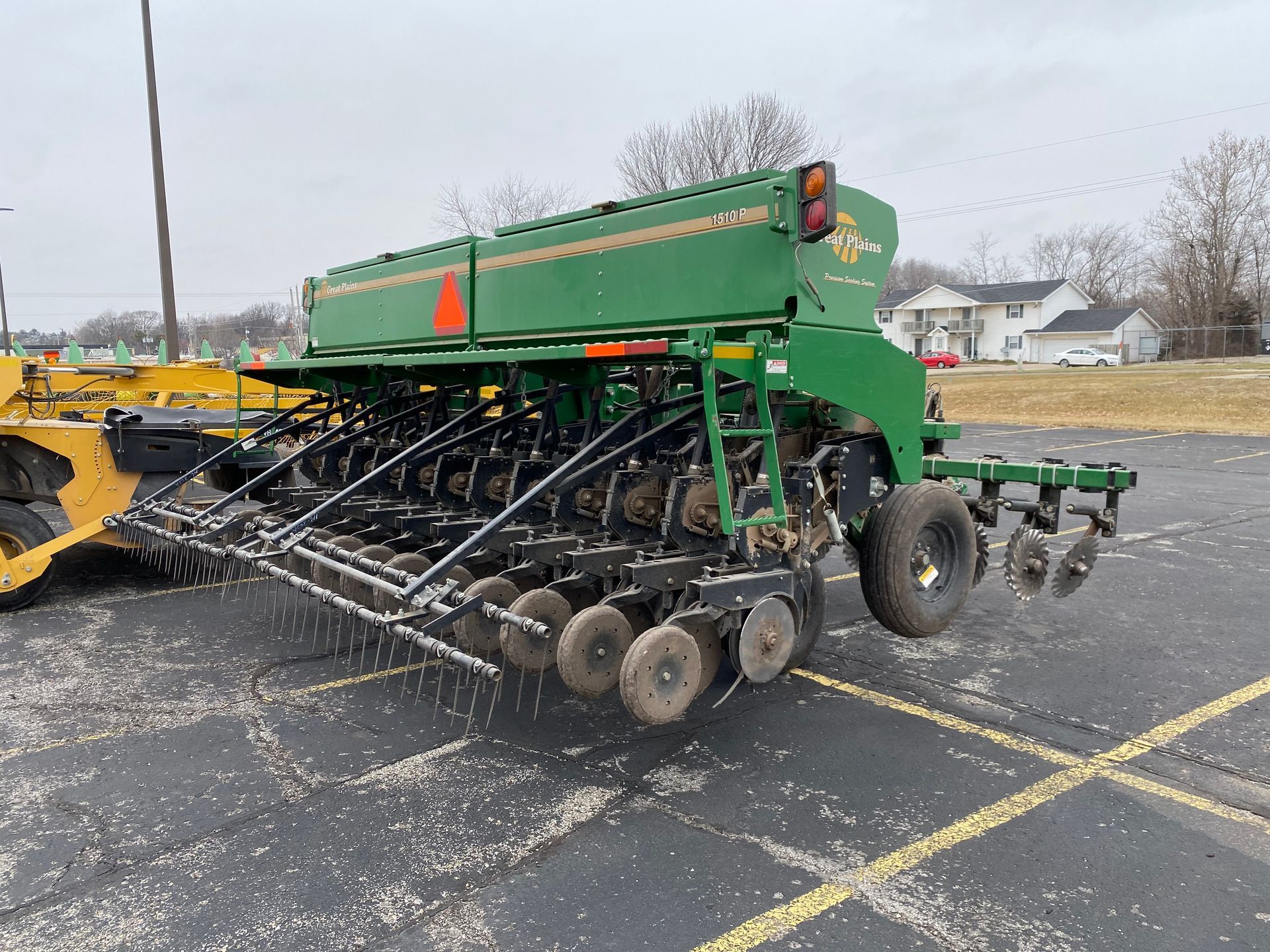 Green agricultural grain drill parked on asphalt, cloudy day, back angled shot.