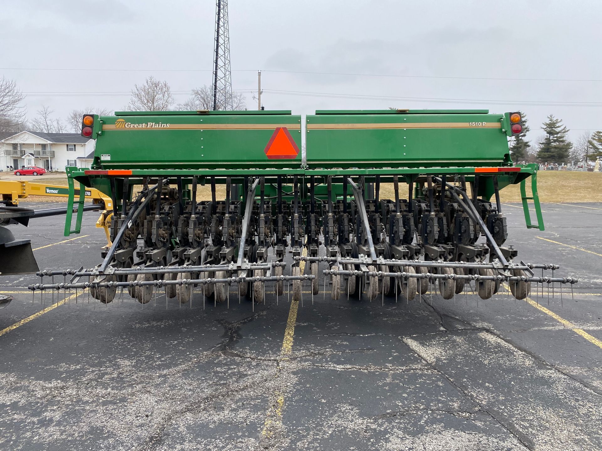 Green agricultural grain drill parked on asphalt, cloudy day, back shot.