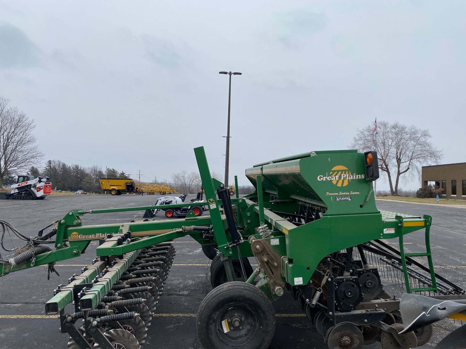 Green agricultural grain drill parked on asphalt, cloudy day, side view shot.