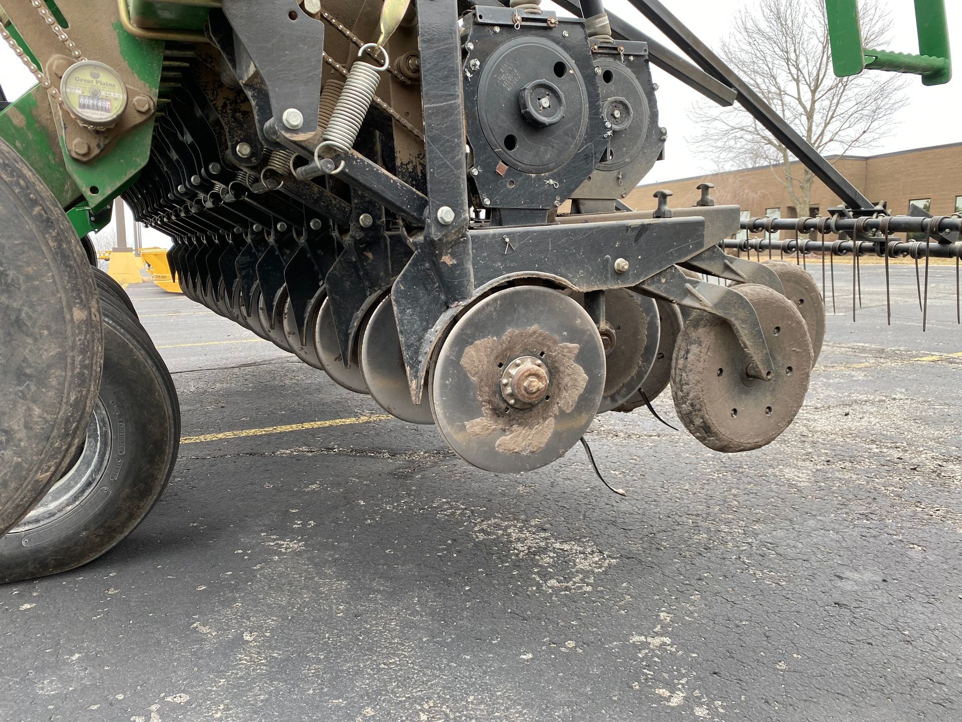 Close-up of a John Deere planter's disc openers and press wheels, positioned on an asphalt surface.