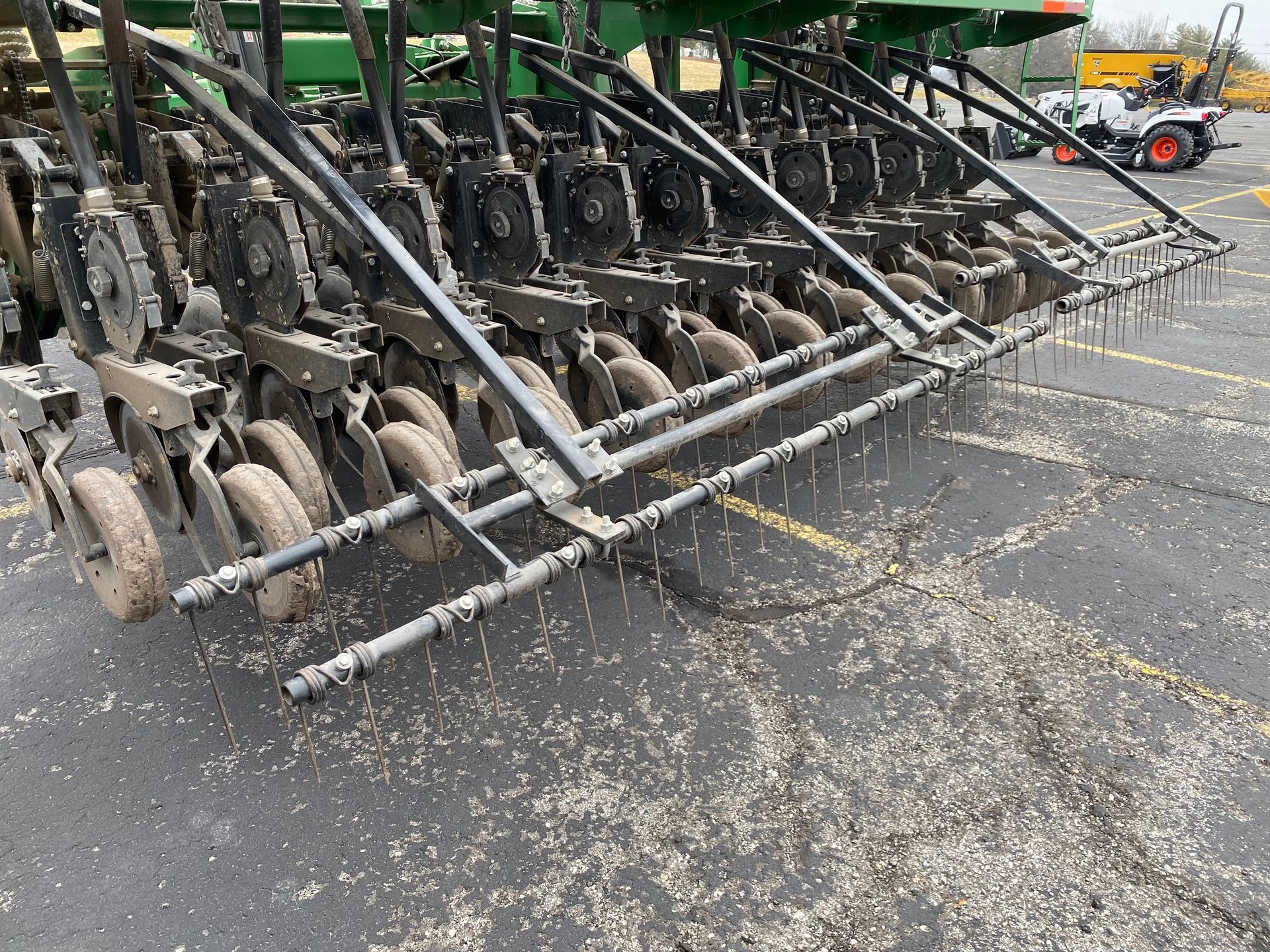 A large agricultural planter with multiple wheels on a paved surface, scattering seeds.
