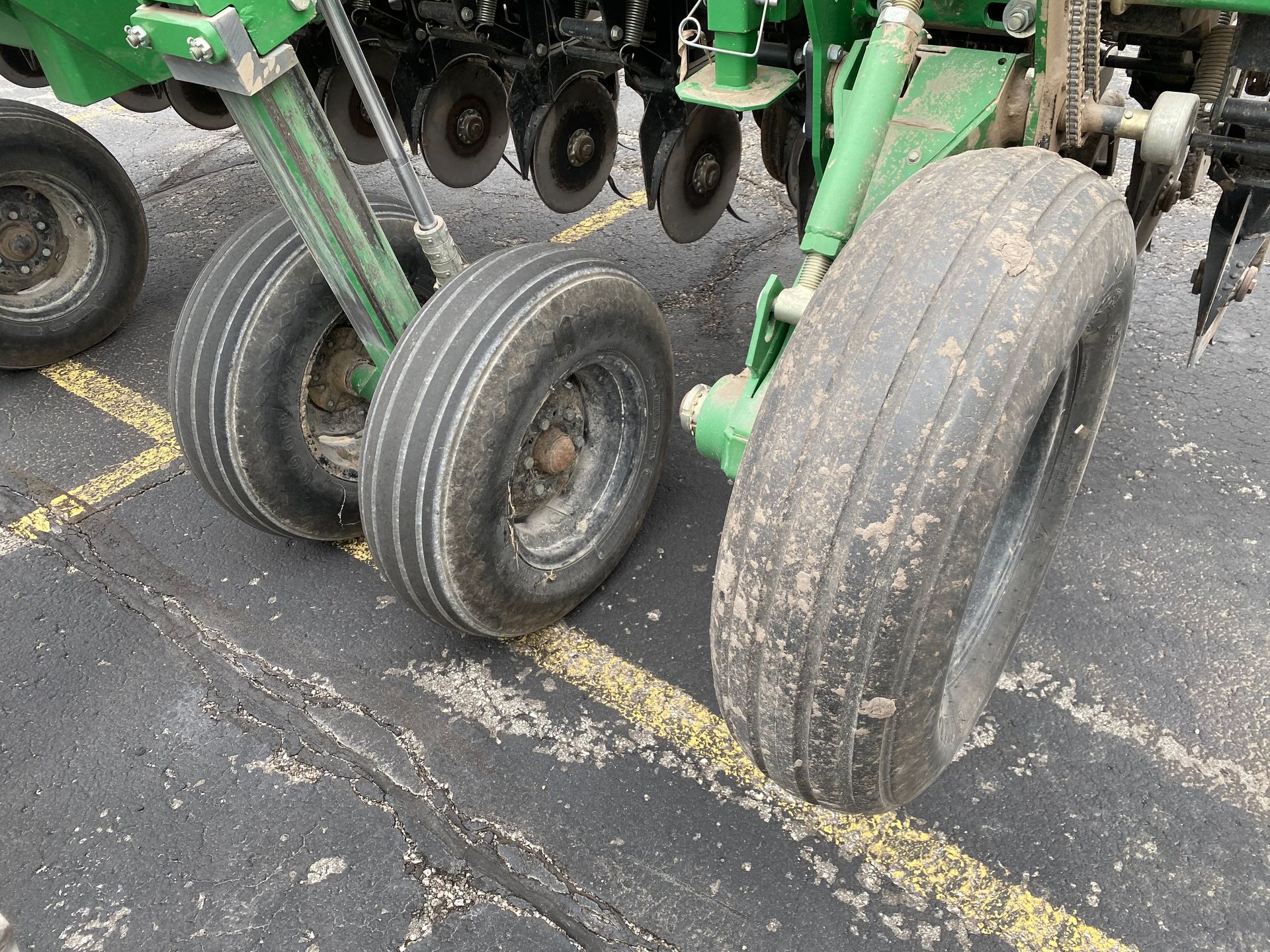 Tires of a green farm implement on asphalt with seed debris.