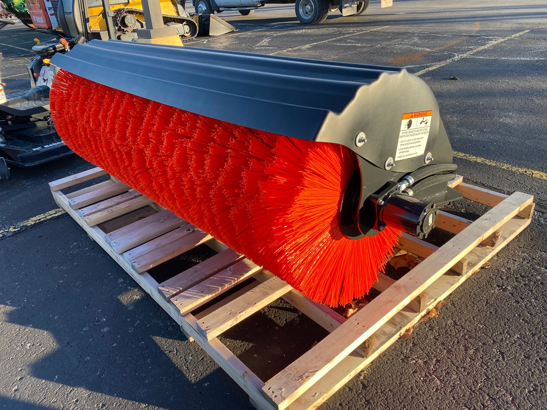 Red and black commercial-grade sweeper brush on a wooden pallet, likely for road or surface cleaning.