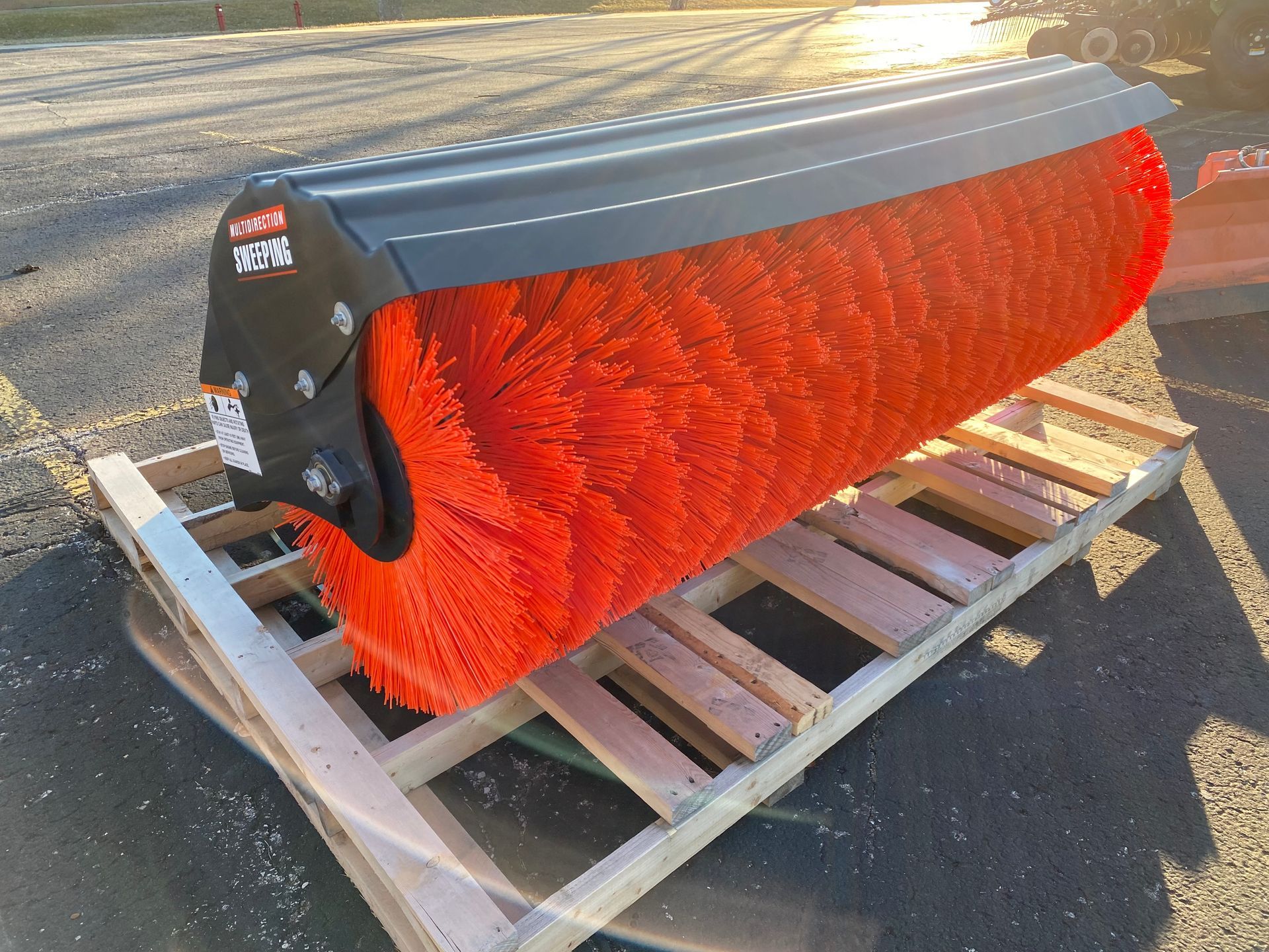 Orange industrial brush attachment on a wooden pallet, outdoors.