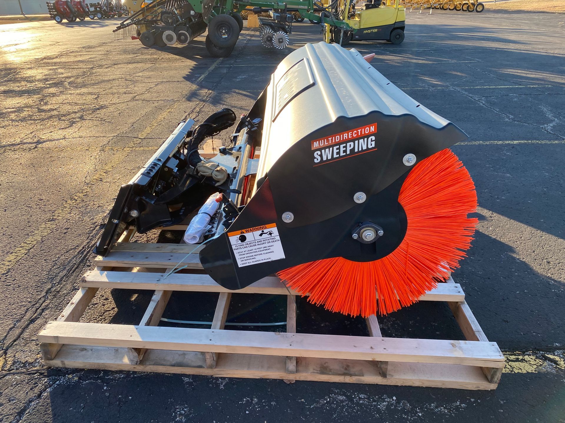 Sweeping attachment with orange brush on a wooden pallet outdoors.