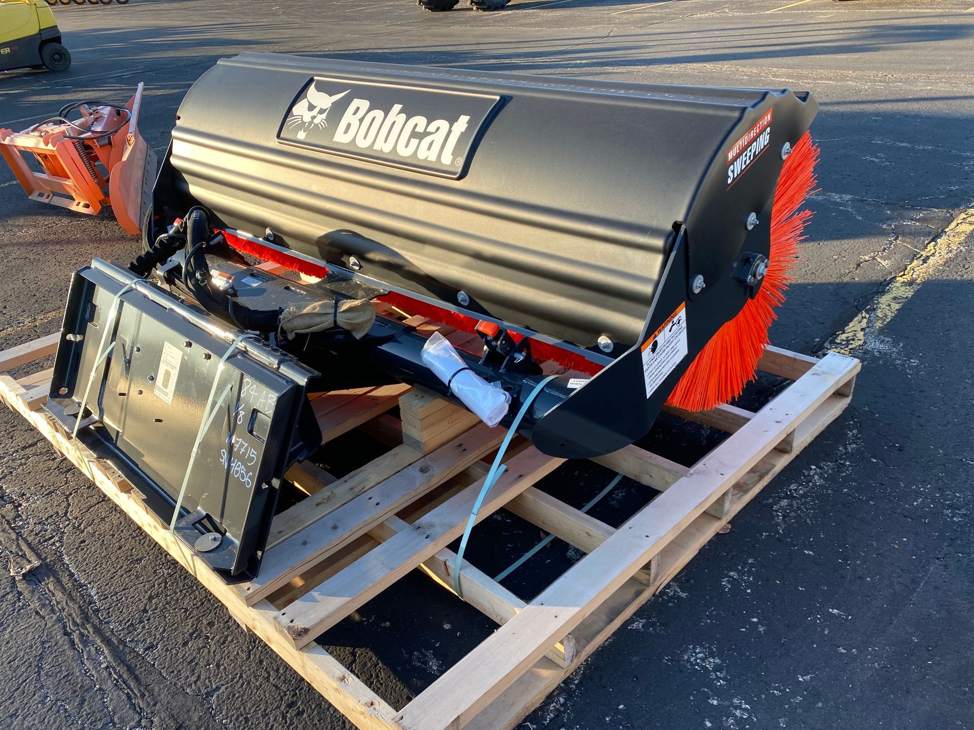 Bobcat sweeper attachment on a wooden pallet; black, with orange brush bristles.