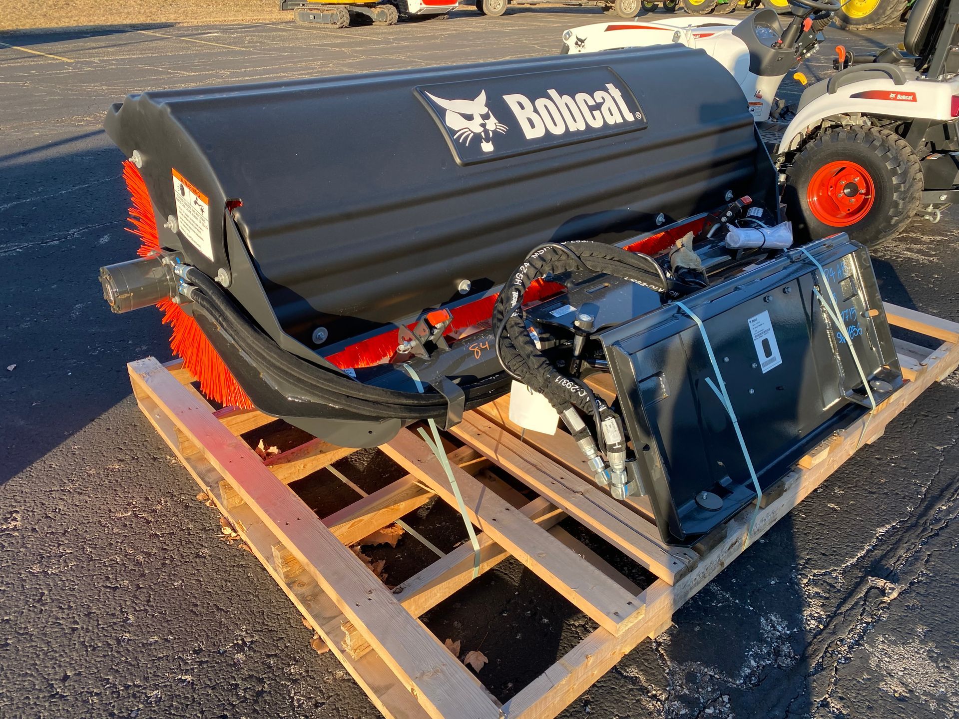 Bobcat brand sweeper attachment on a wooden pallet, black and orange, ready for use.