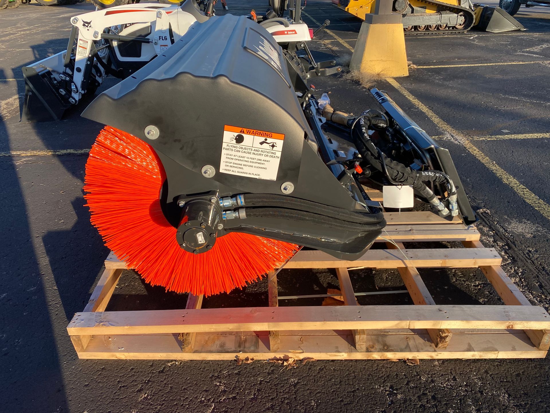 Bobcat sweeper attachment with orange bristles on wooden pallet outdoors.